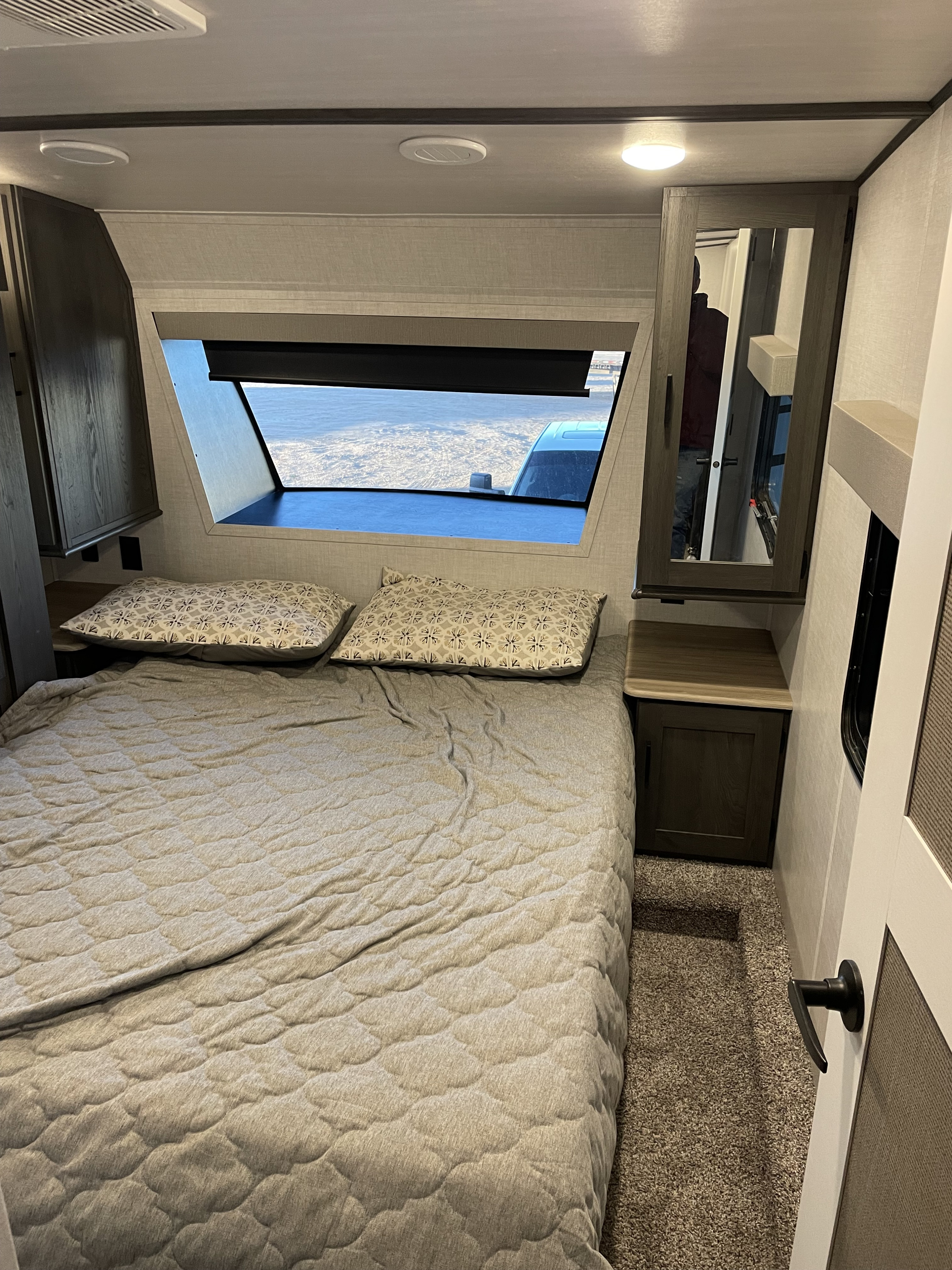 Cozy RV rental bedroom with a bed, wide window, bedside tables, and a mirrored cabinet.. Forest River Impression 2024