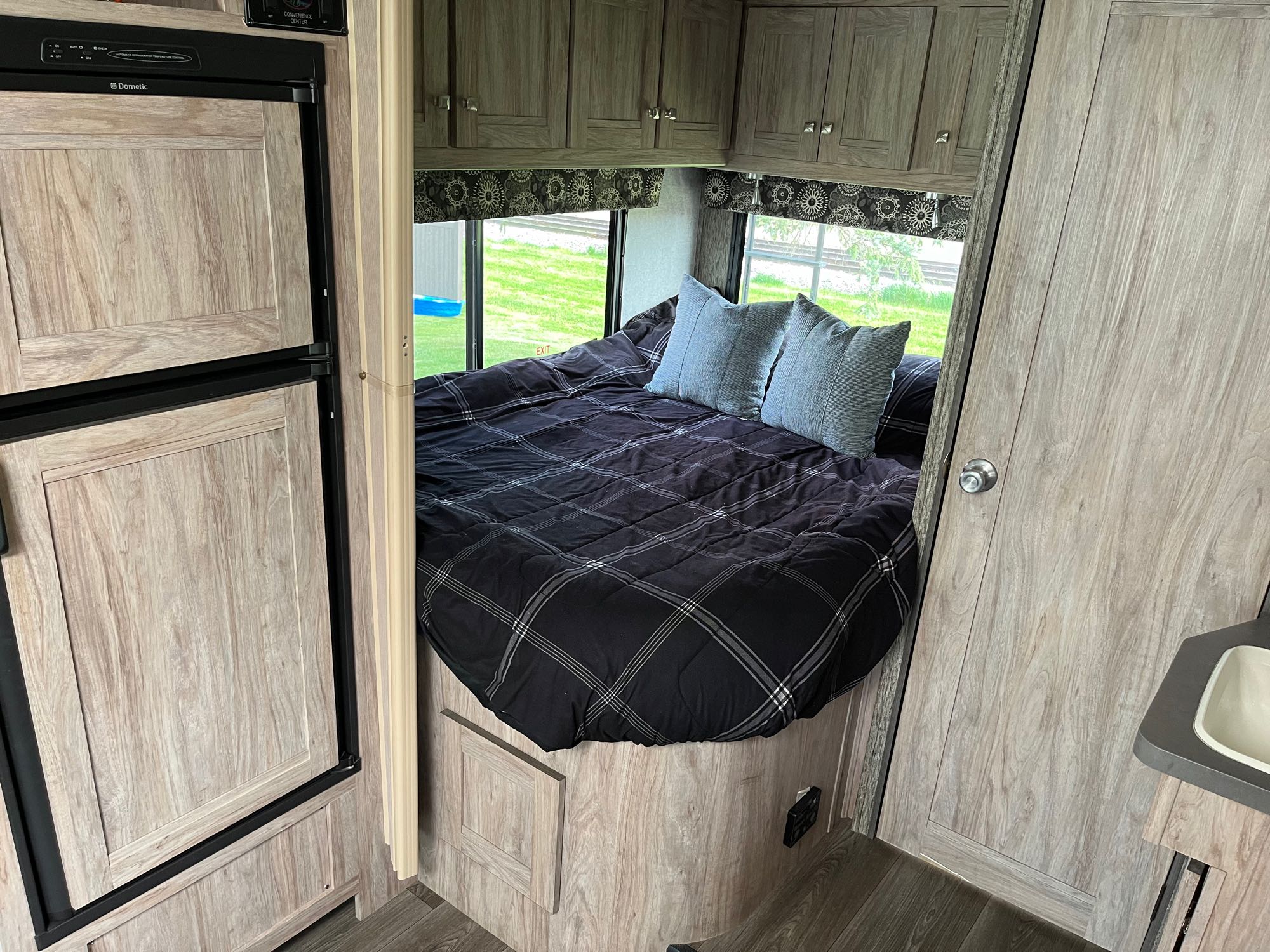 Interior of an RV rental: a cozy bedroom with a large bed, plaid comforter, and windows offering scenic views. Storage cabinets visible.. Forest River Sunseeker MBS 2017