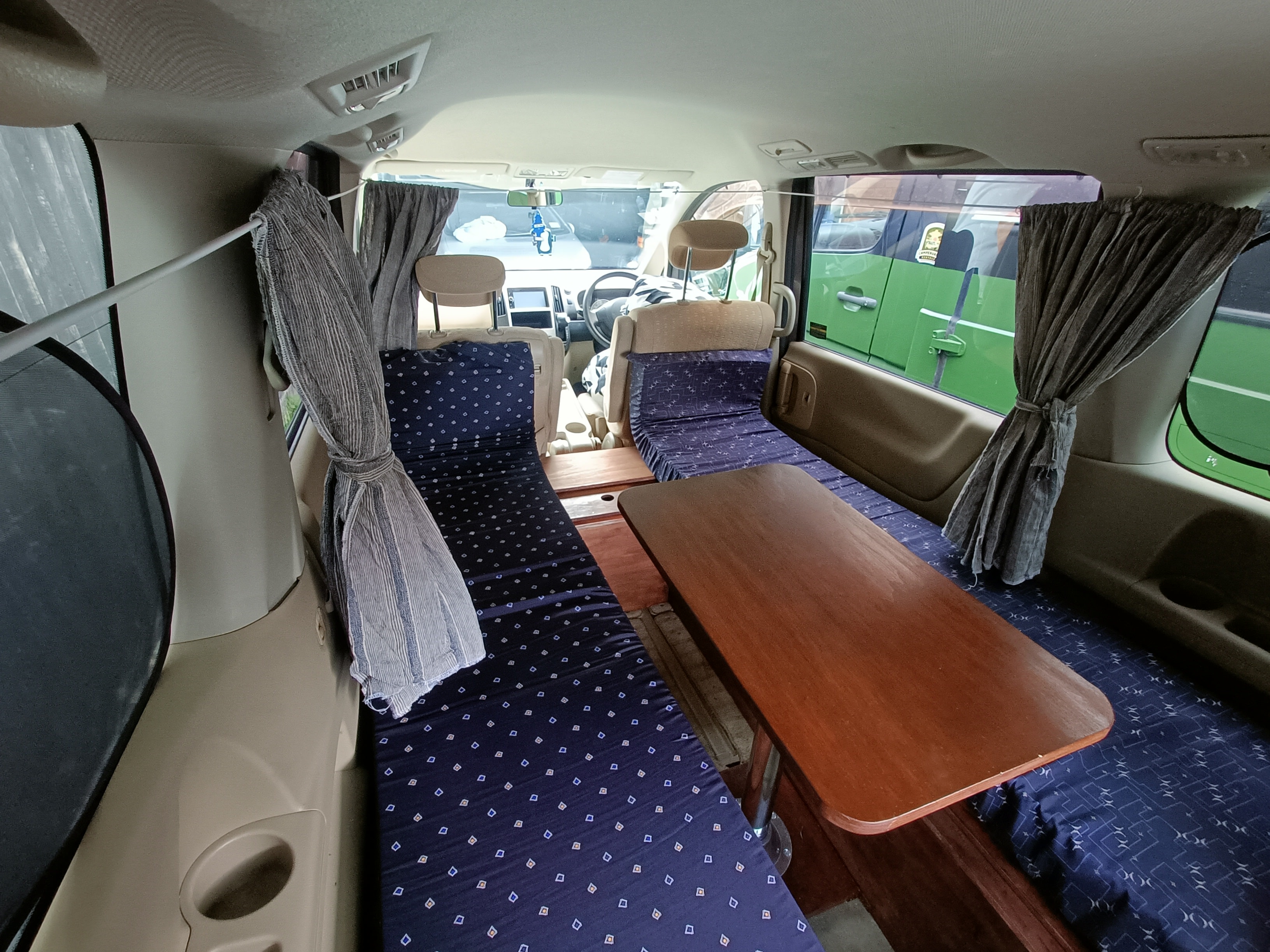 Cozy RV rental interior: Camper van with two beds/seating, a wooden table, and privacy curtains. Ready for travel!. nissan Serena 2007