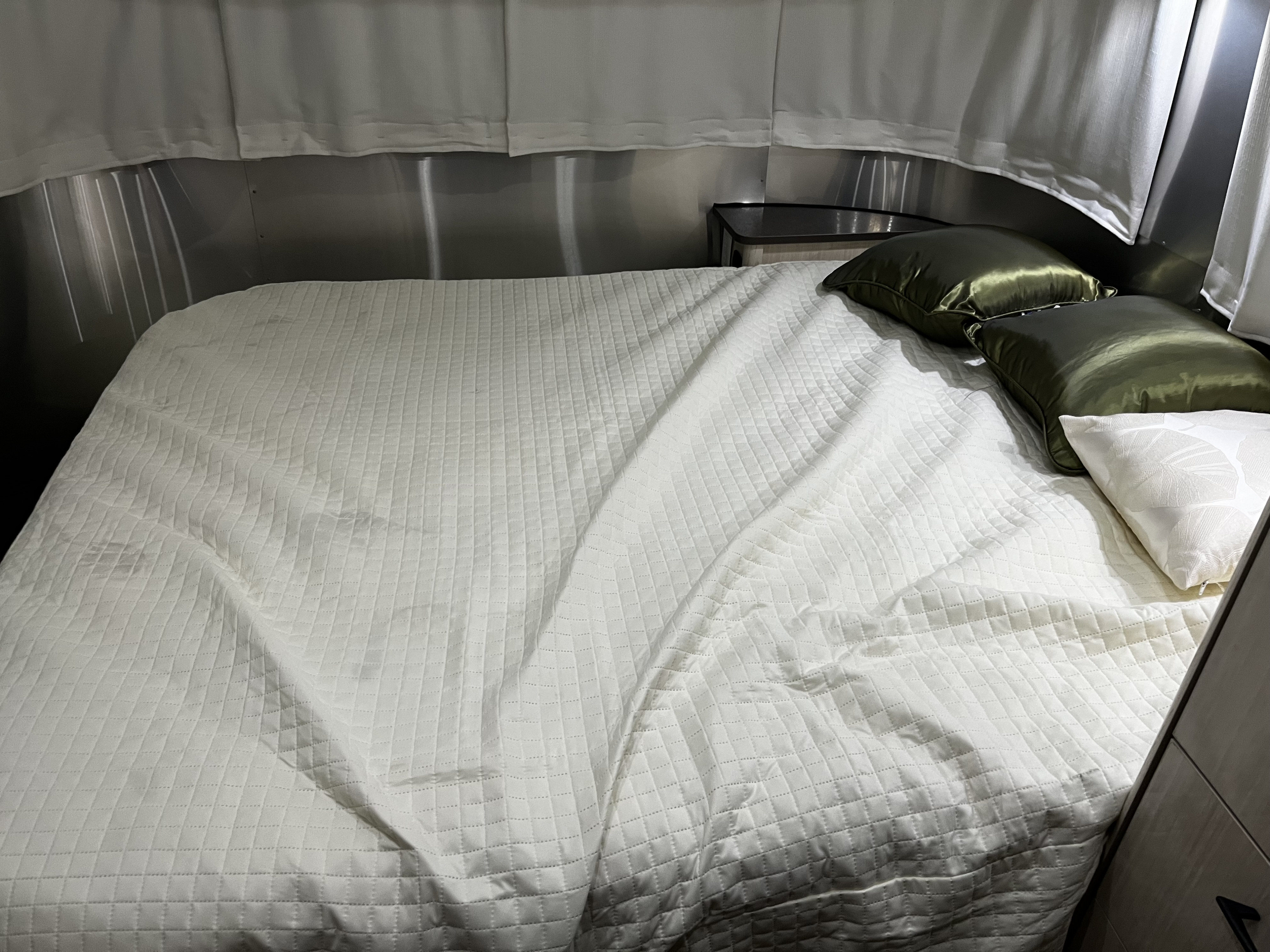Comfortable RV rental bed with white quilted bedding and green pillows, set against metallic walls.. Airstream International 2017