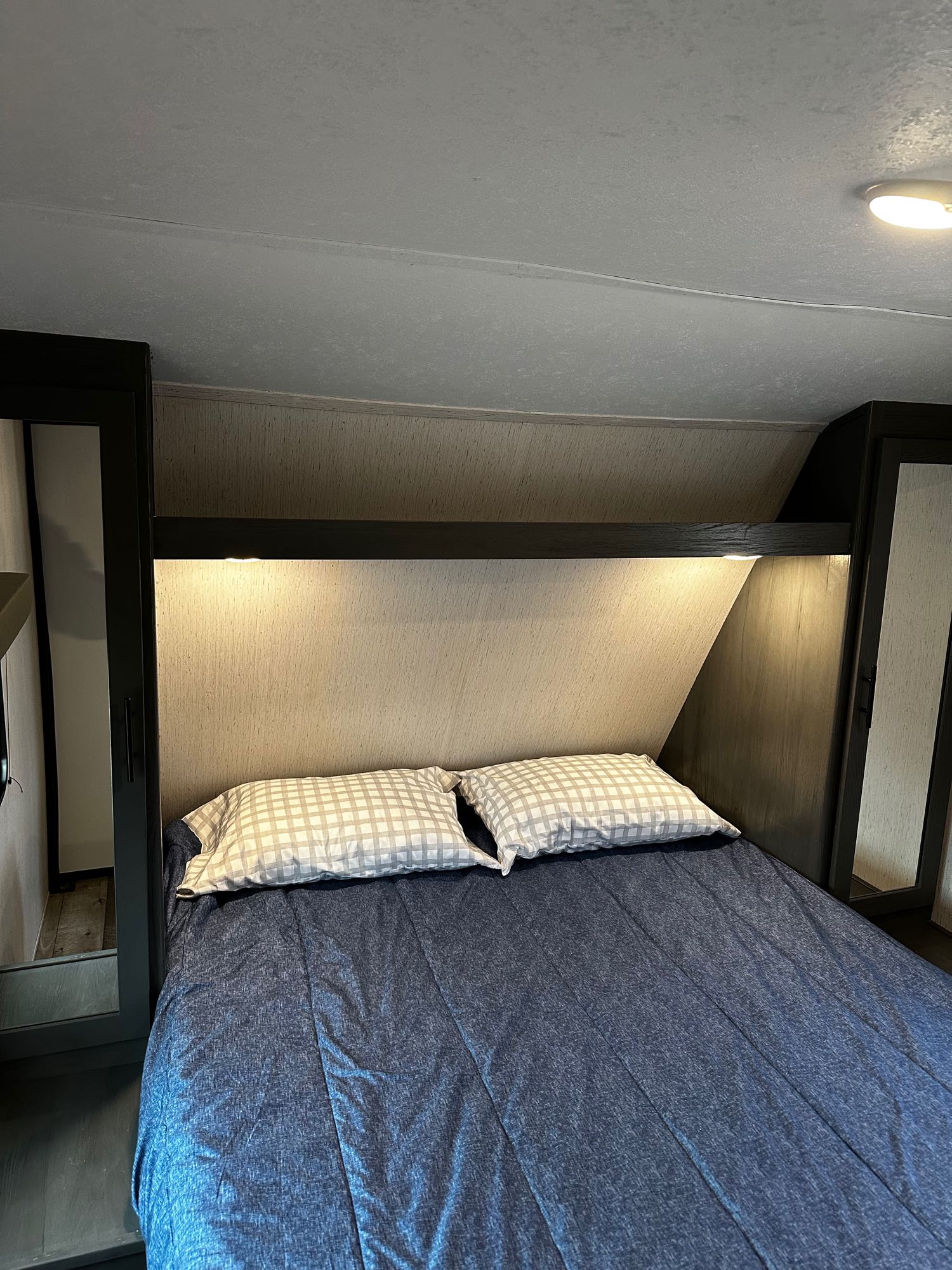 RV rental bedroom: a comfortable bed with blue bedding, plaid pillows, integrated lighting, and side cabinets for storage.. Aspen Trail Dutchmen 2022
