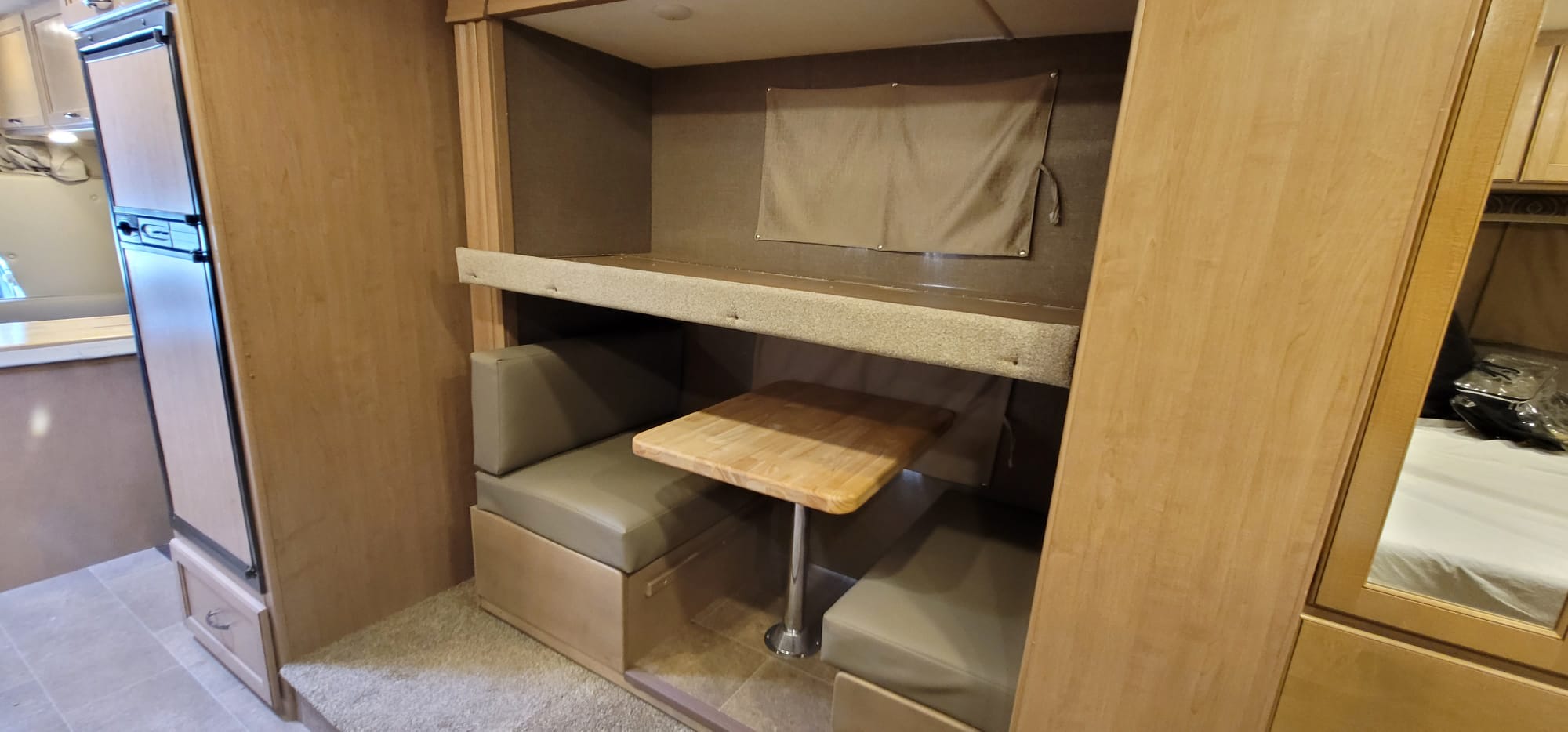 RV rental interior showcasing a cozy dinette with table & benches, convertible bunk bed, and fridge.. Thor Chateau 2018