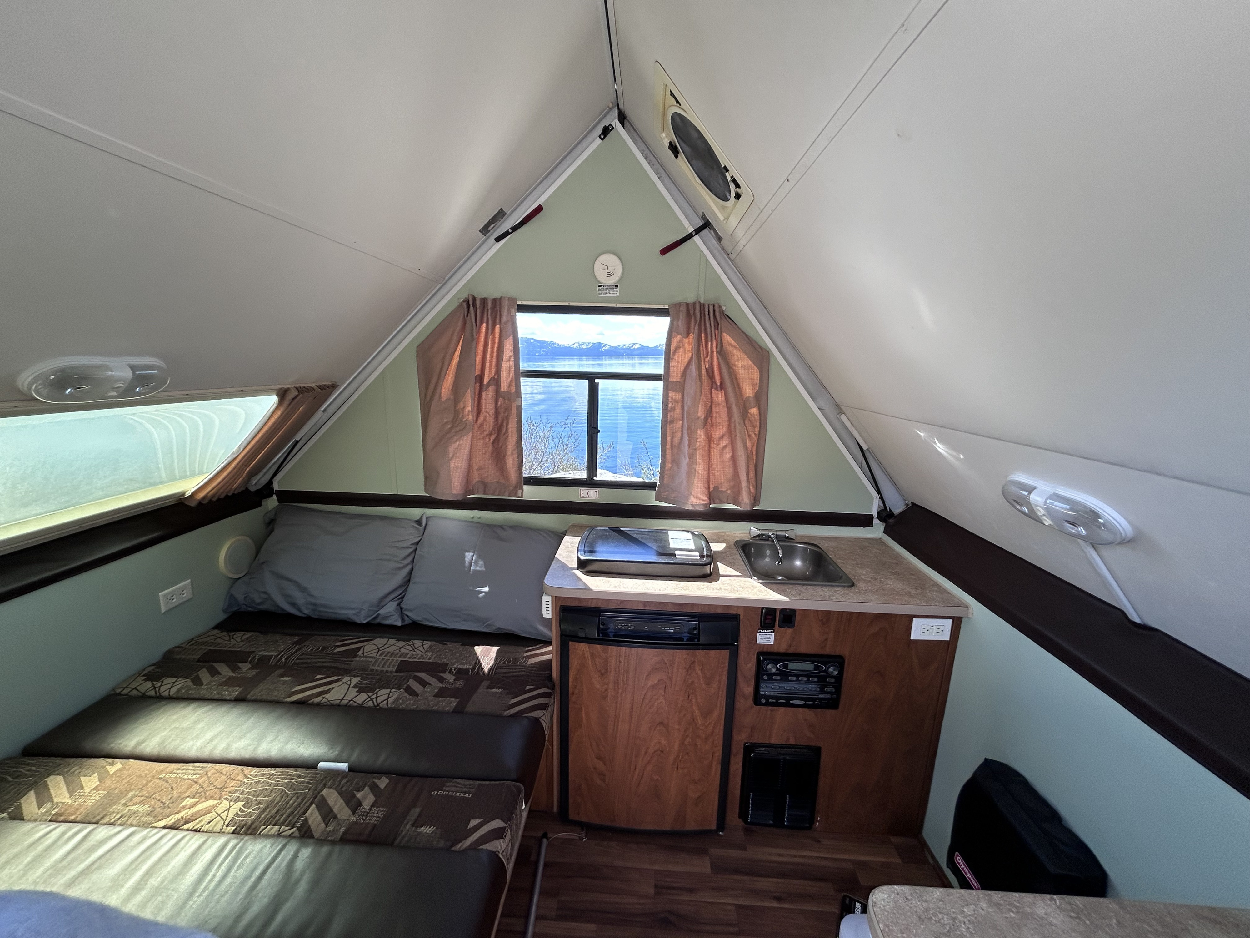 Cozy RV rental interior: bed, compact kitchen, and a stunning lake and mountain view from the window.. Chalet Chalet Popup Trailer 2013