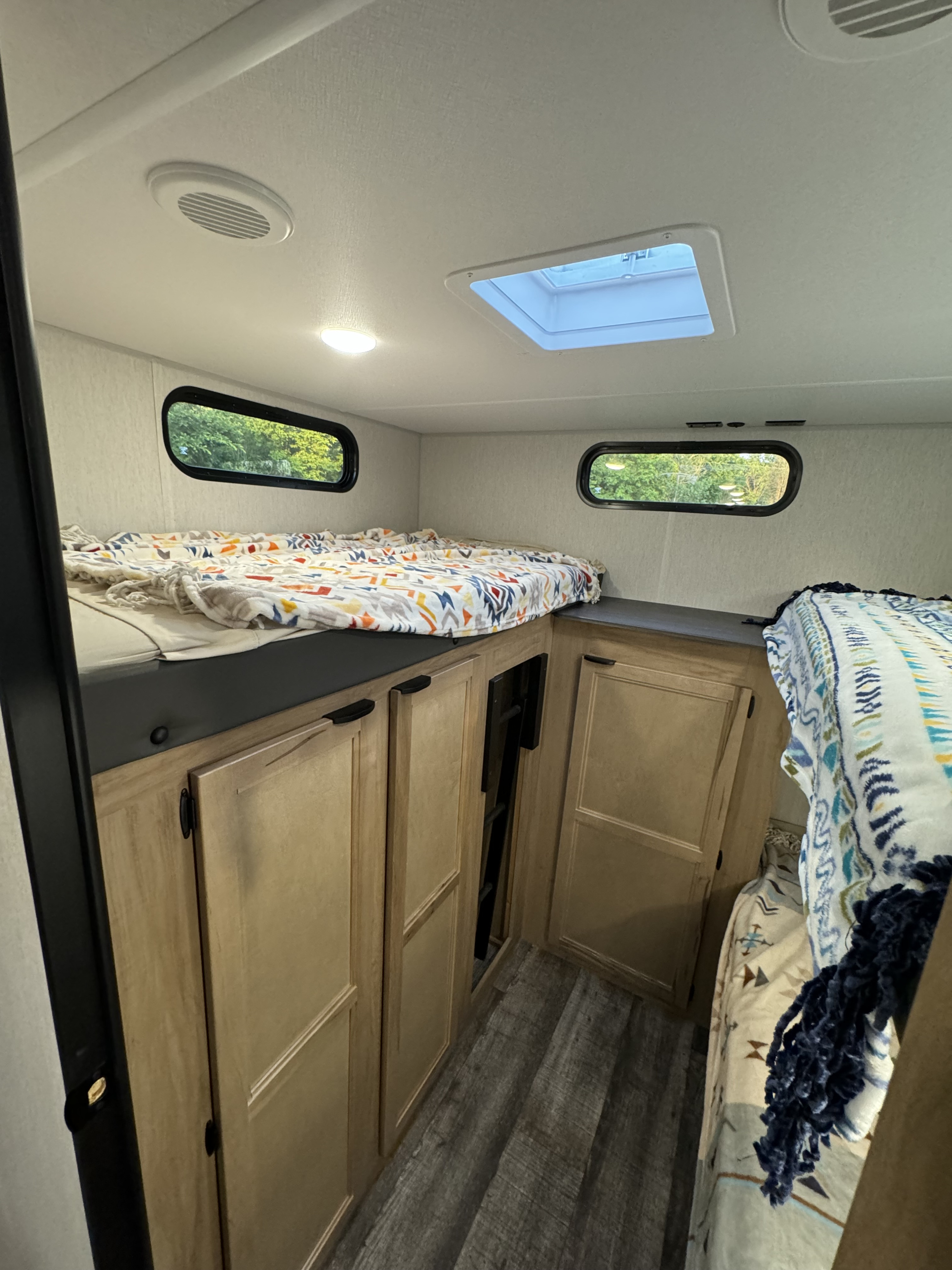 Inside an RV rental, showing the bunk bed sleeping area with blankets, storage cabinets, and natural light from windows and a skylight.. Forest River Grey Wolf 29TE 2024