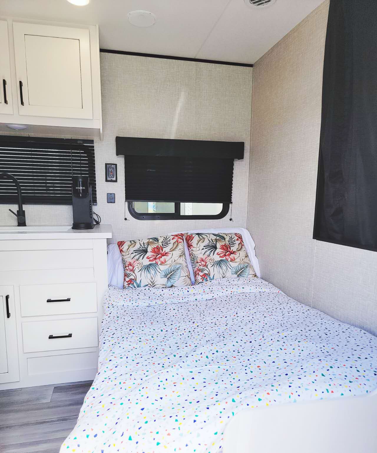 Cozy RV rental interior showing a compact bedroom with floral pillows & a small kitchenette area.. Jayco Jay Flight SLX 2024