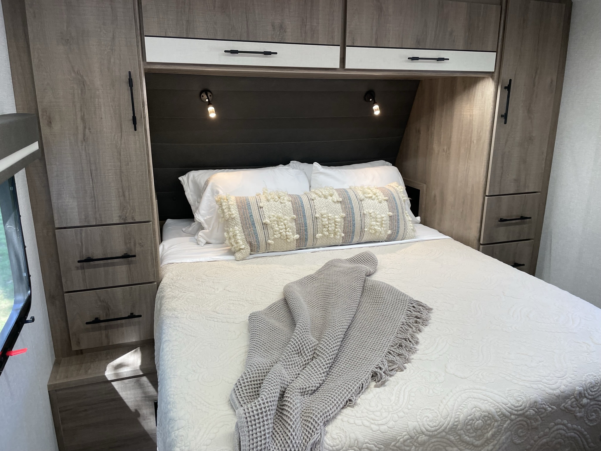 Experience comfort in this RV rental bedroom: a modern space with a comfy bed, functional storage, and warm lighting.. Grand Design Imagine XLS 2024