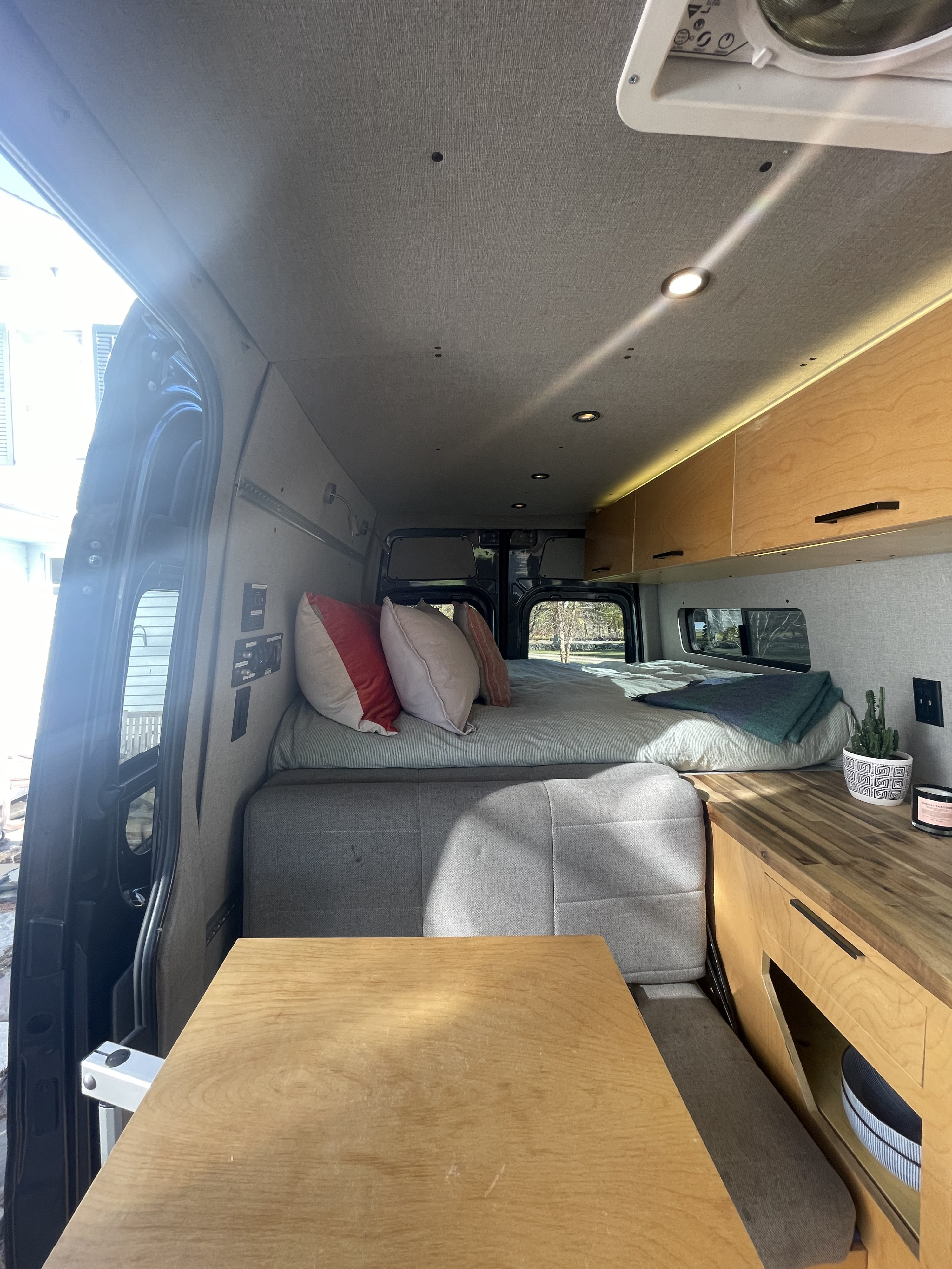 Bright RV rental interior with a cozy bed, seating, and wooden kitchen counter, ideal for travel.. Mercedes-Benz Sprinter 2020