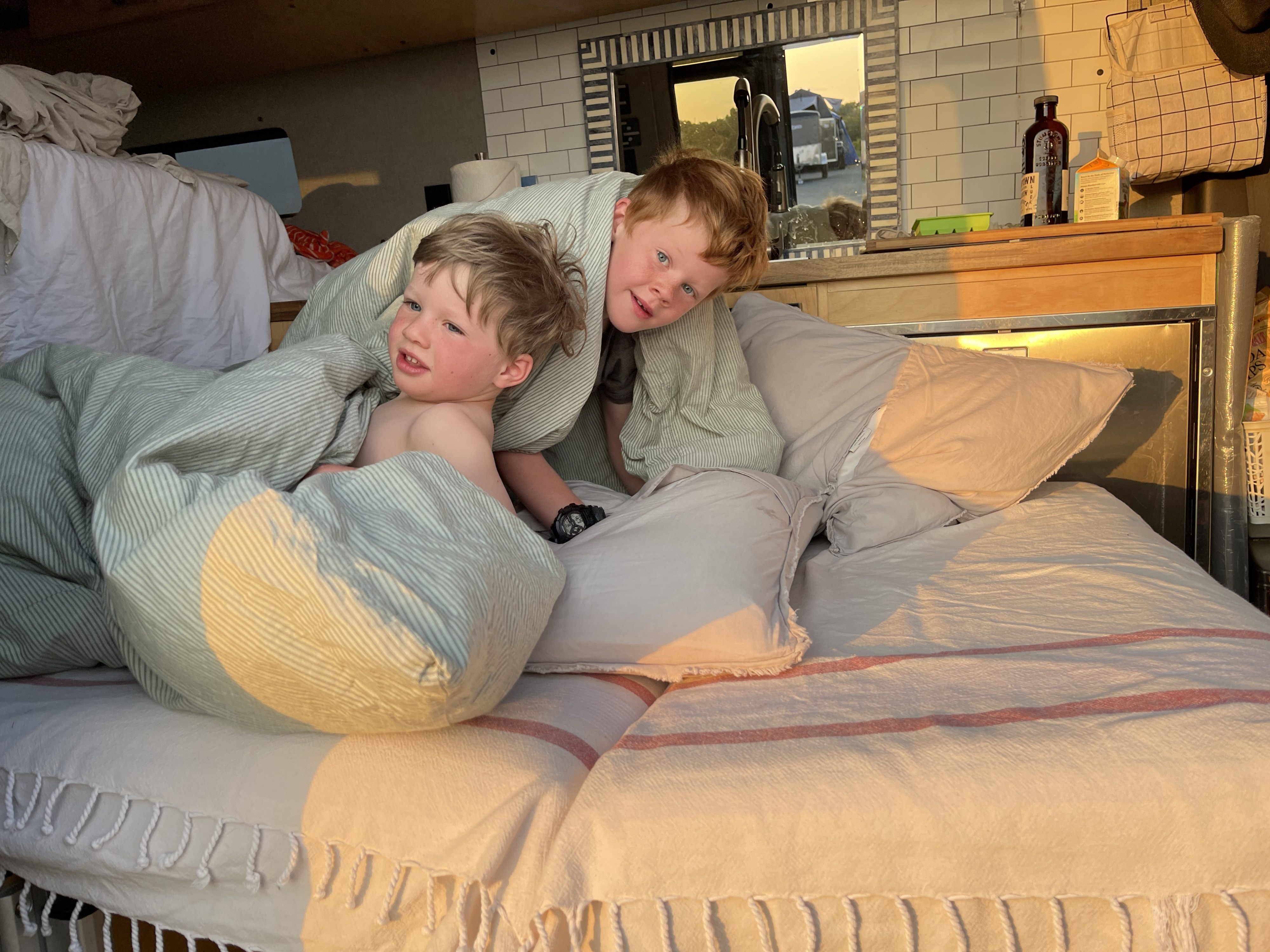 Two boys wake up cozy in their RV rental bed, sunlight streaming in.. Mercedes-Benz Sprinter 2020