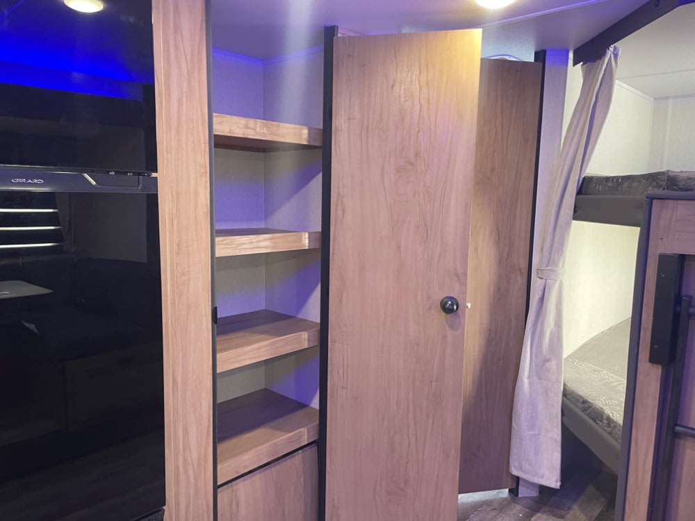 Explore this RV rental's interior: a TV entertainment area, built-in shelving, and cozy bunk beds with privacy curtains.. Forest River Grey Wolf 26 DBH 2024