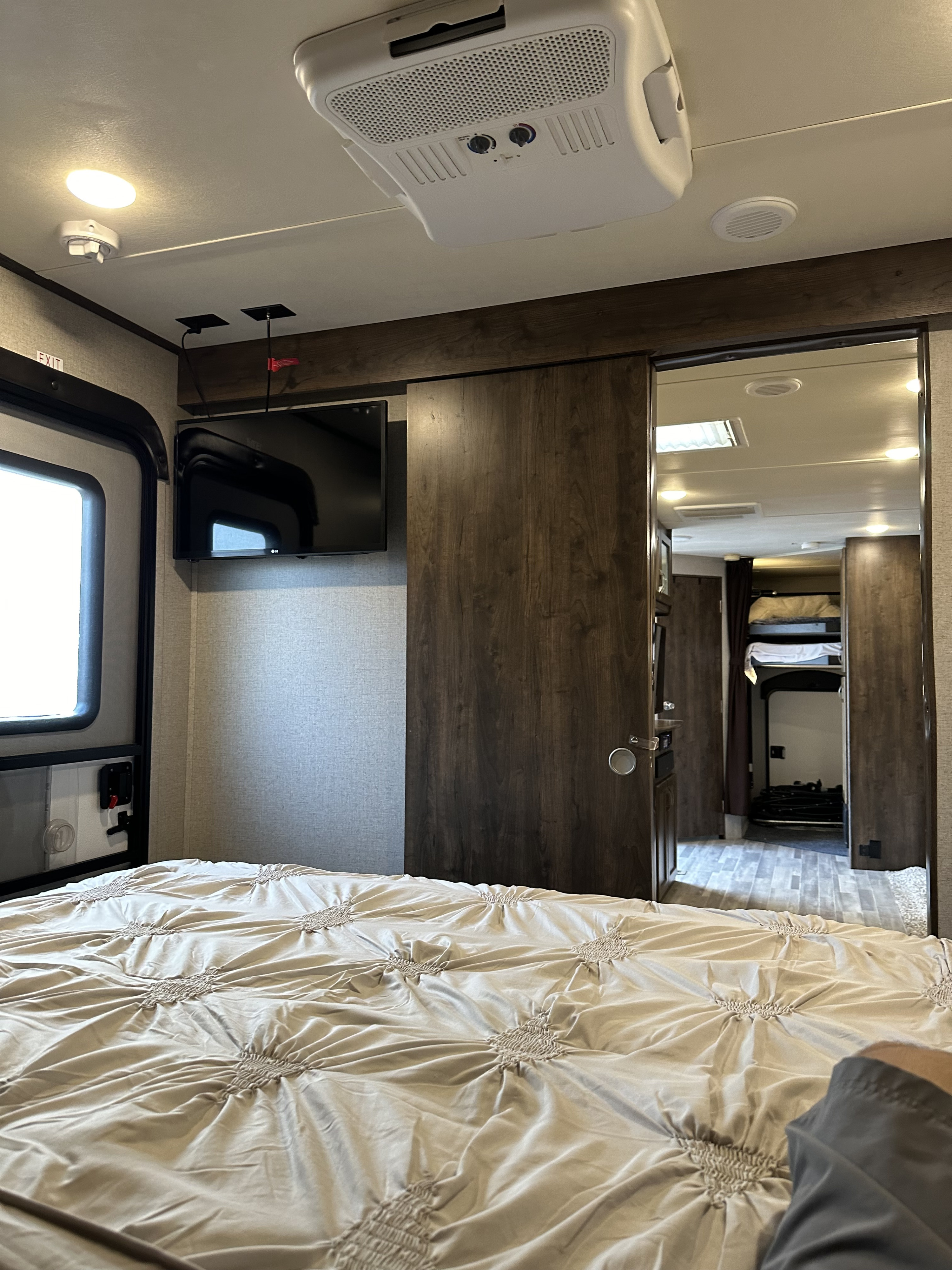 An RV rental's cozy bedroom features a large bed, ceiling AC unit, wall TV, and a sliding door leading to bunk beds.. Dutchmen 4yYDT28427JP911000 2018