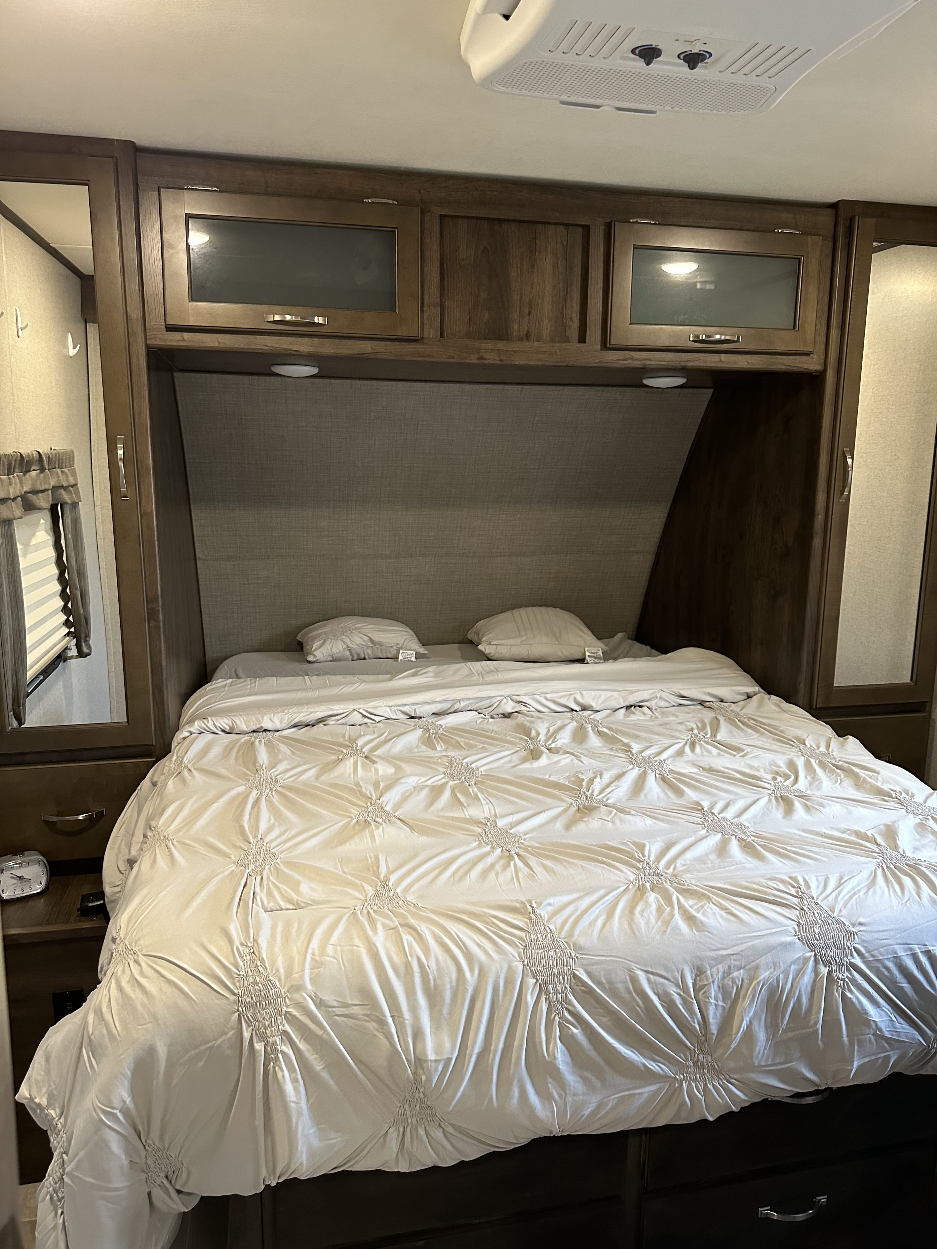 RV rental bedroom with a large bed, light comforter, pillows, wooden overhead cabinets, and ceiling AC unit. Includes side storage.. Dutchmen 4yYDT28427JP911000 2018