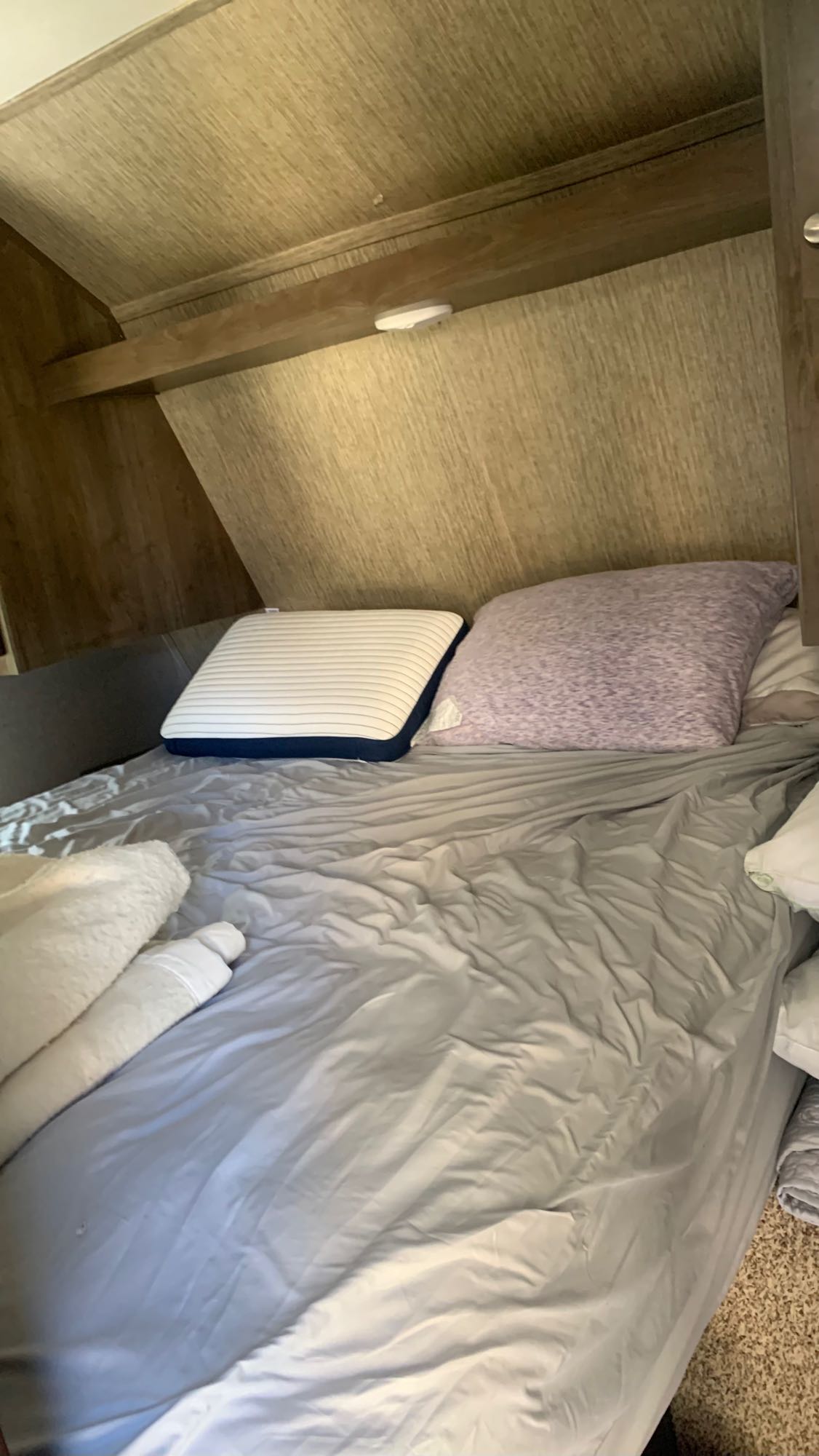 RV rental bedroom features a cozy bed with light gray sheets, two pillows, and wood-paneled walls. Perfect for travel lodging.. Dutchmen Coleman Lantern 2019