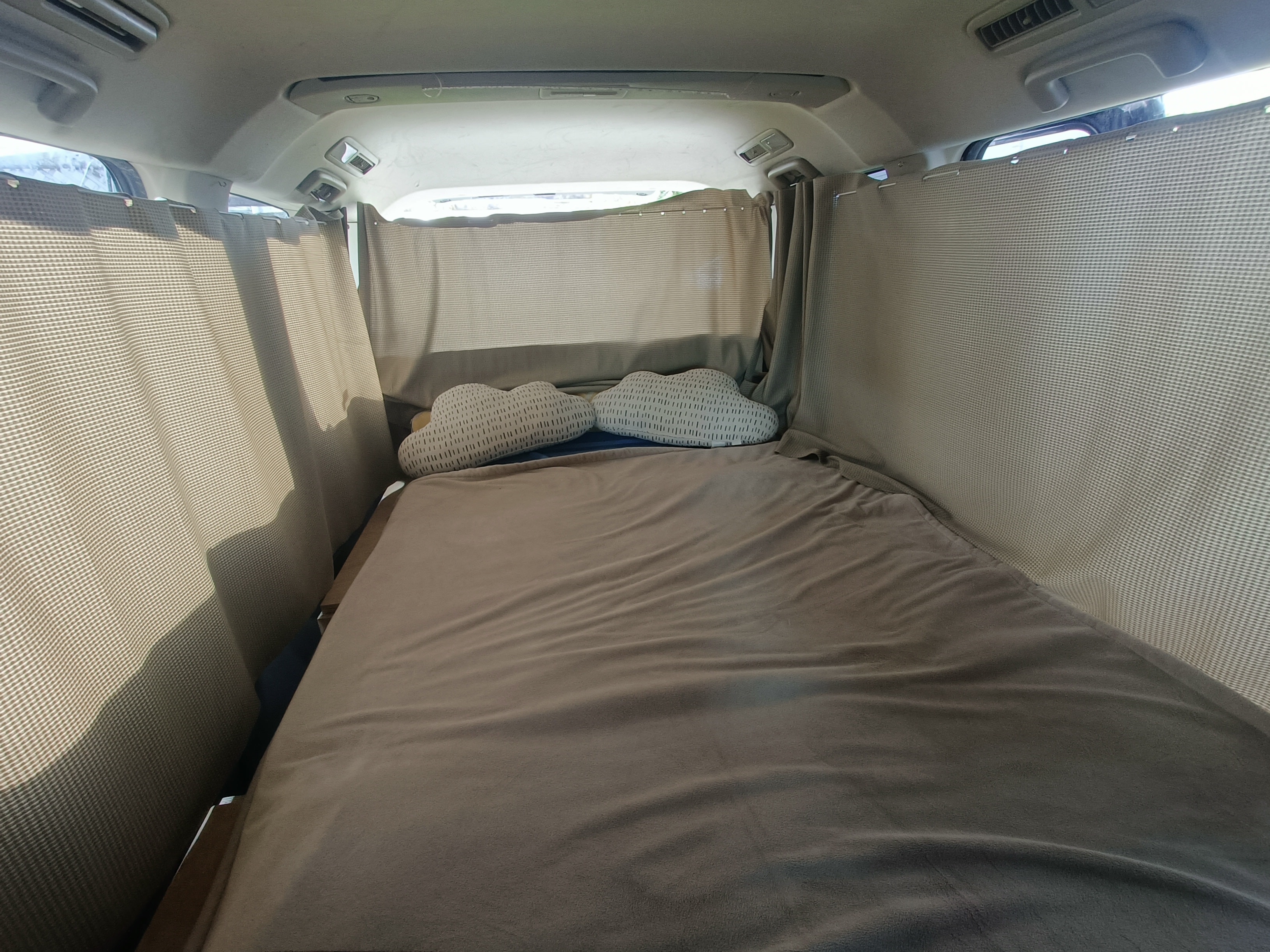 Inside an RV rental, a snug bed with cloud pillows and privacy curtains creates a comfy sleeping area for travelers.. Mitsubishi Delica 2007