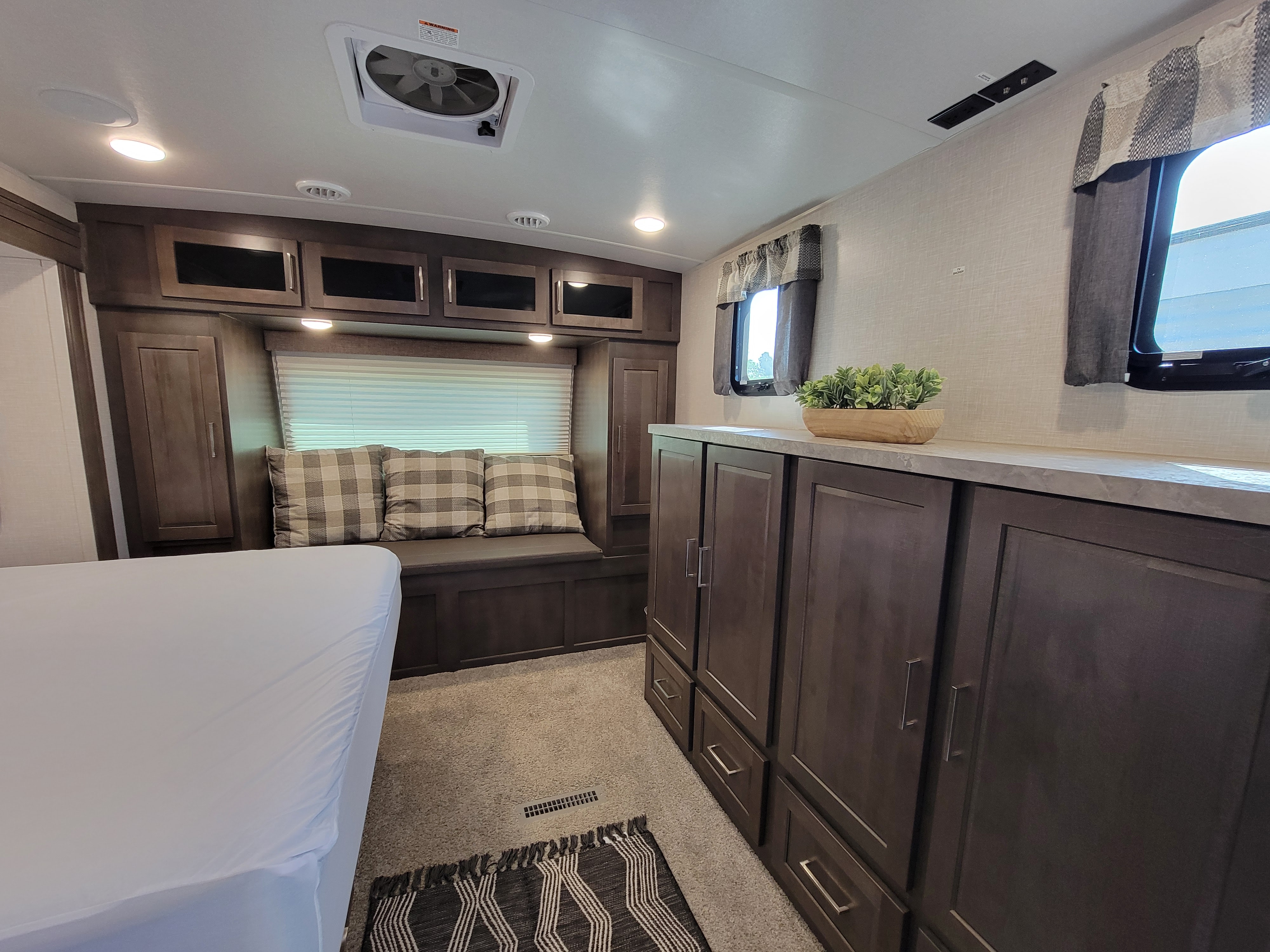 Explore this cozy RV rental interior: a bed, bench seating with pillows, dark wood cabinets, and bright windows.. Forest River Flagstaff Super Lite 2021