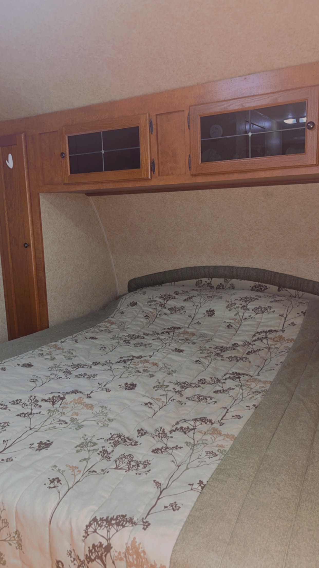 Comfortable RV rental bedroom showing a bed with a floral quilt, wooden overhead cabinets, and side closet. Ideal for travel.. Layton Joey 2011