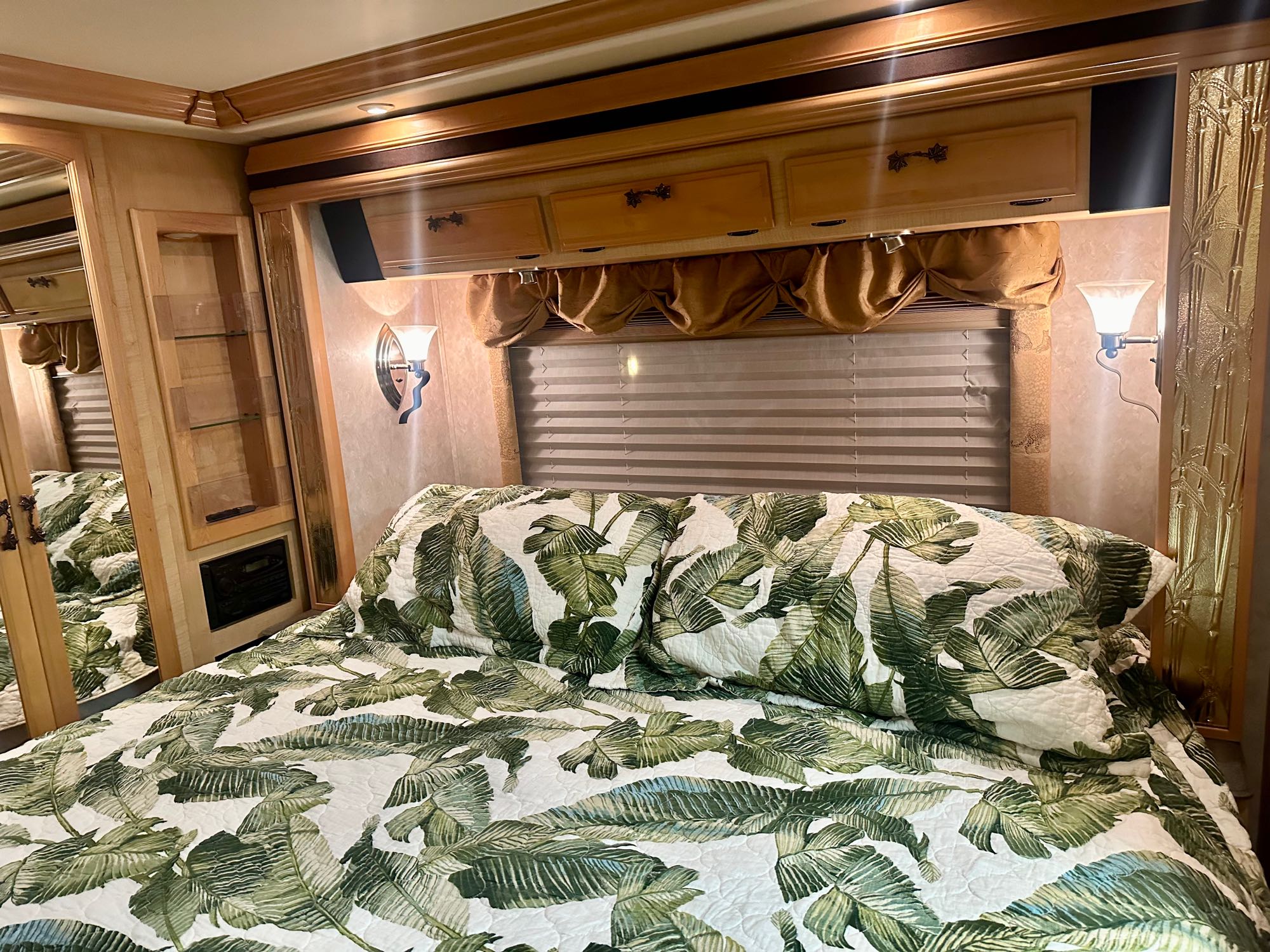 Cozy RV rental bedroom features a tropical leaf quilt, overhead storage, and warm lighting, ideal for travel.. Fleetwood Excursion 39s 2005