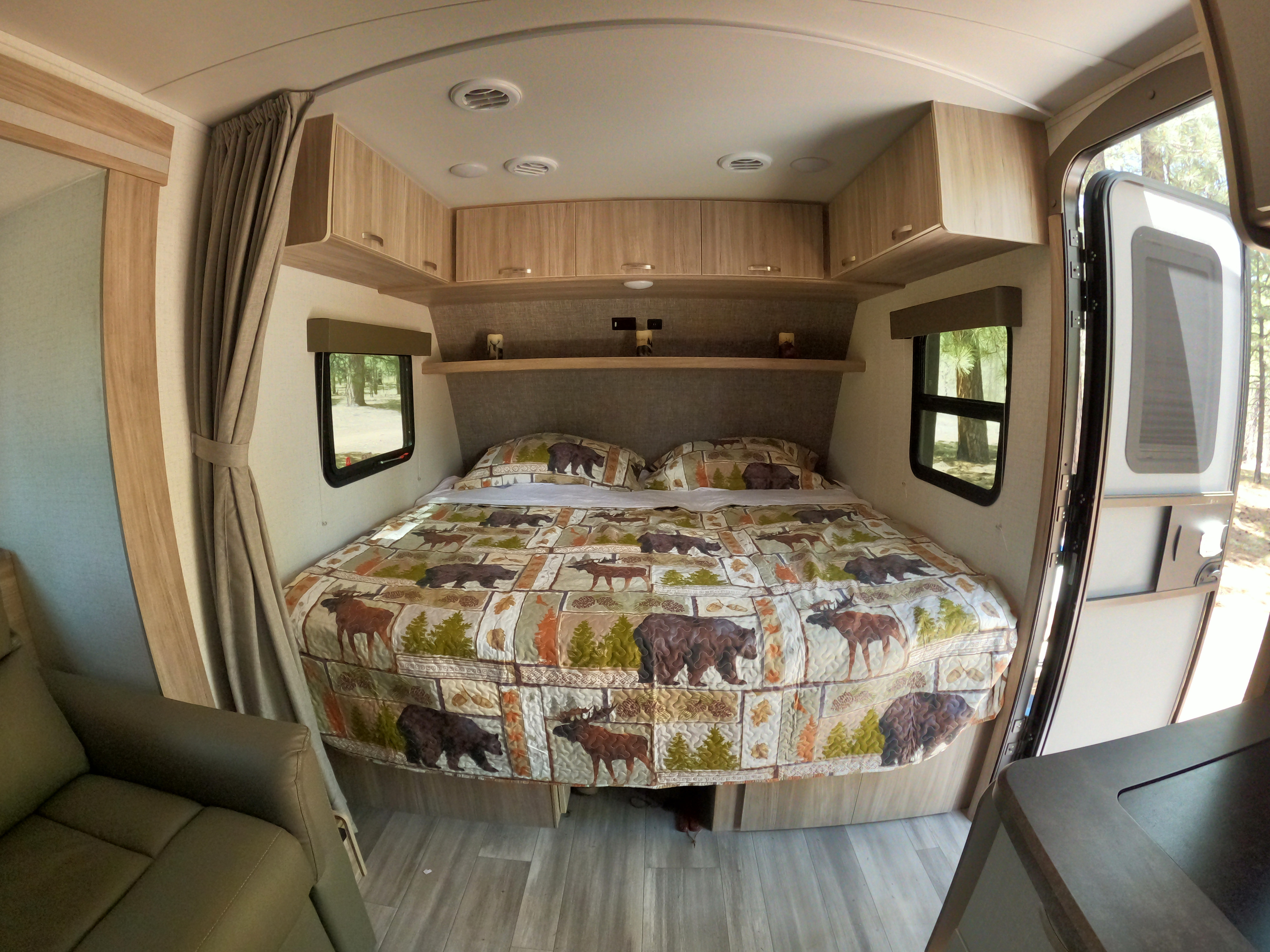 Spacious RV rental bedroom featuring rustic wildlife quilt, cabinets, and outdoor views for your next adventure.. Winnebago Micro Minnie 2022