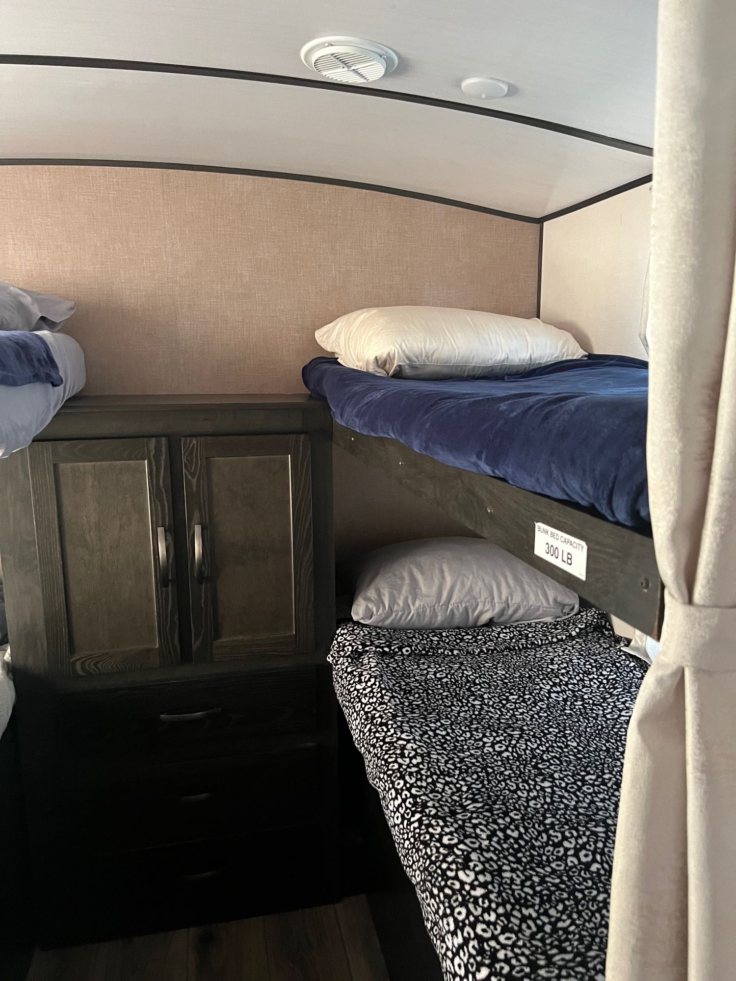 Inside an RV rental: cozy bunk beds with a cabinet & drawers. Upper bunk capacity is 300 lbs.. Forest River Surveyor Legend 2019