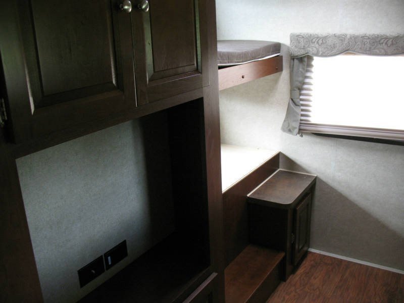 Experience comfort in this **rv rental**! Dark wood cabinets, a cozy bunk bed, and a window with blinds make a snug camper interior.. Forest River Rockwood Signature Ultra Lite 2015