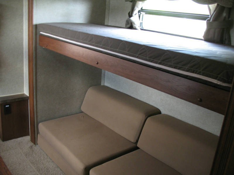 Cozy RV rental interior: upper bunk bed, lower sofa seating, and window. Ideal compact living space for road trips.. Forest River Rockwood Signature Ultra Lite 2015