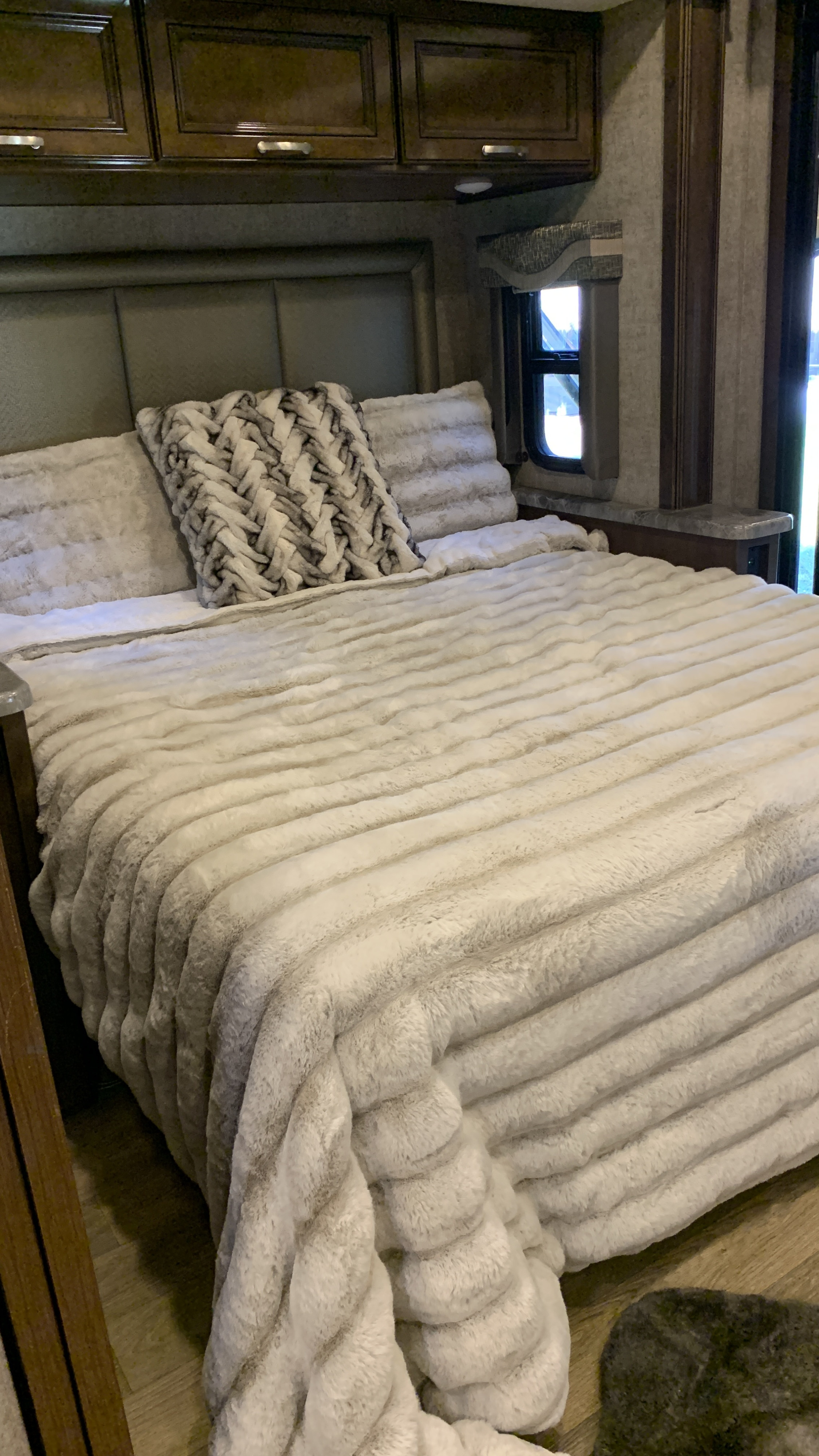 Cozy RV rental bedroom with a plush white bed, braided pillow, and dark wood cabinets. Comfortable interior for your travels.. Thor Outlaw 2020