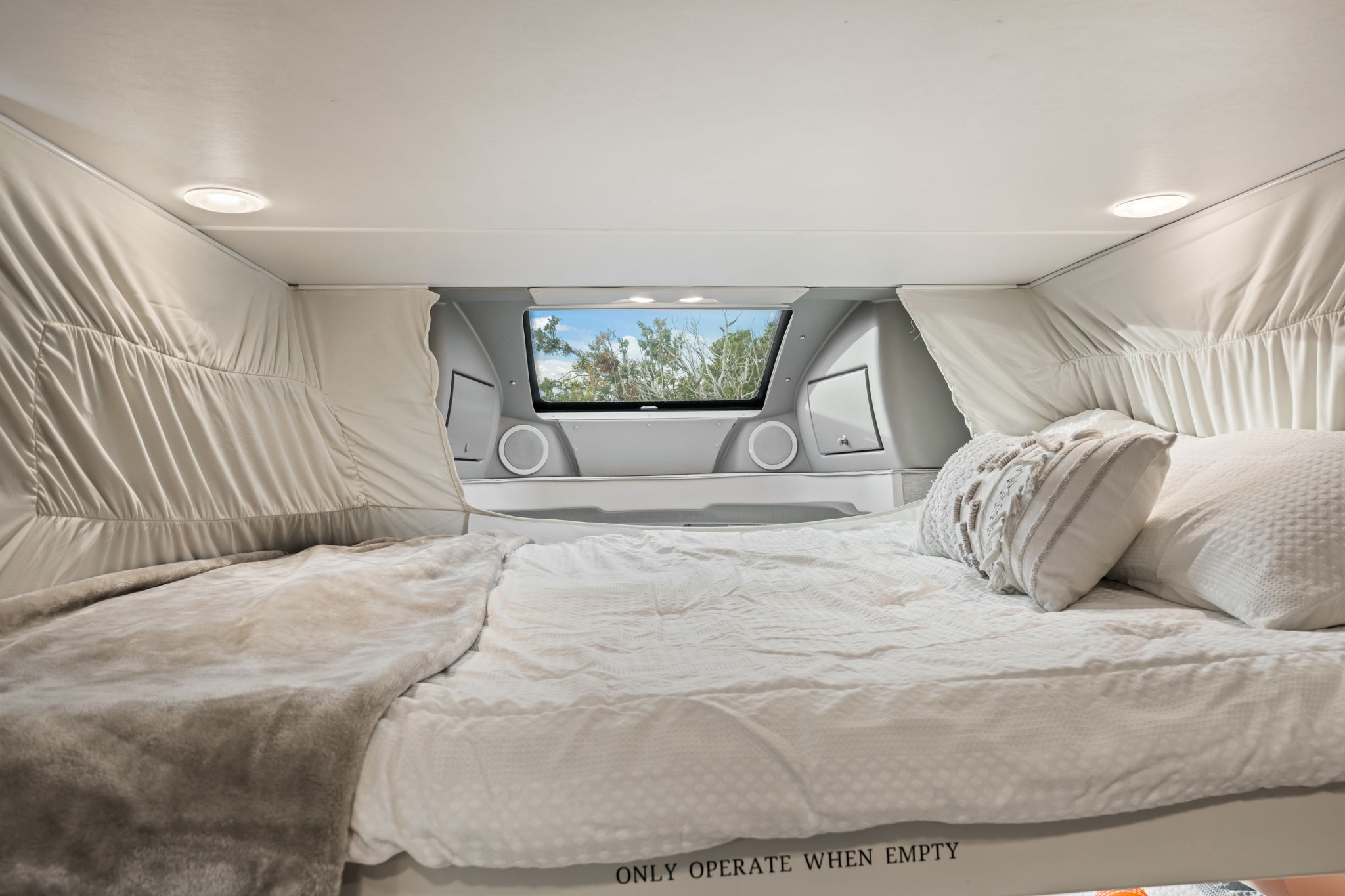 Comfortable RV rental sleeping area with soft bed, window view of trees, and integrated speakers. Ready for your next trip!. Winnebago Trend 2015