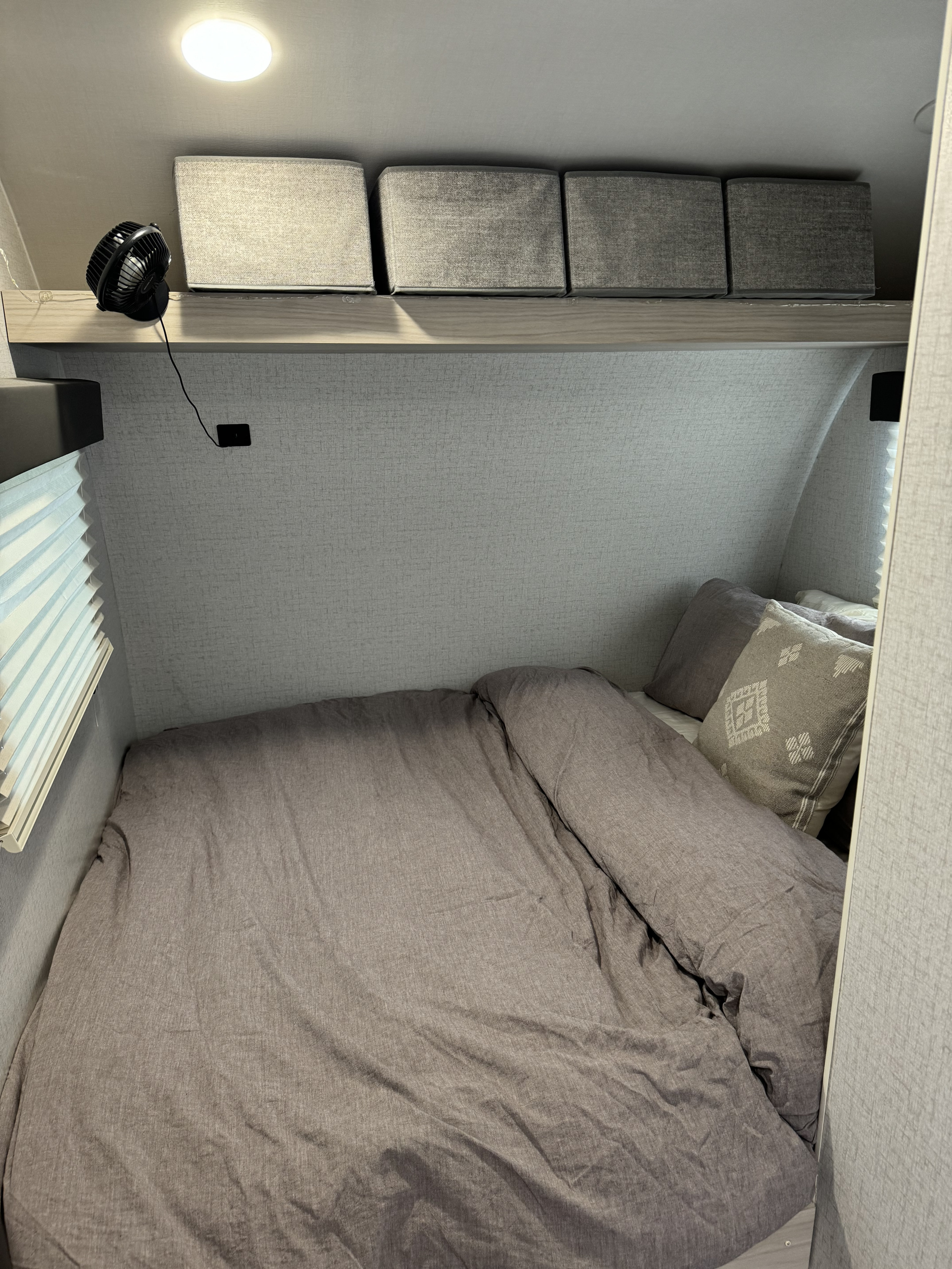 RV rental bedroom: cozy space featuring a bed, grey bedding, overhead shelf with storage, and a small fan.. Winnebago Hike 2021