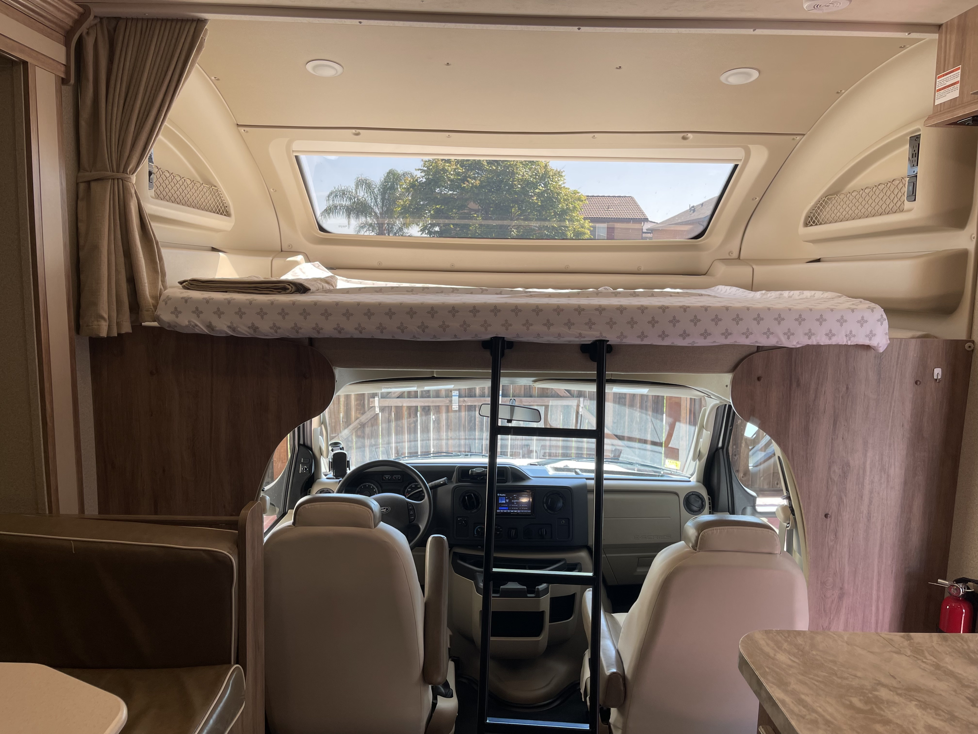 Bright RV rental interior shows a neatly made overhead bunk bed, ladder, and front cockpit area with seating.. Entegra Coach Odyssey 2019