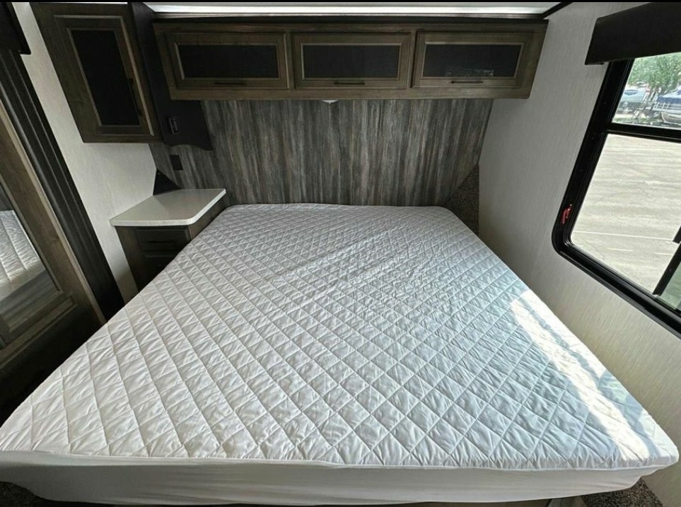 Bright RV rental bedroom featuring a white quilted bed, dark wood cabinets, and an outside view from the window.. Heartland Cyclone 2022