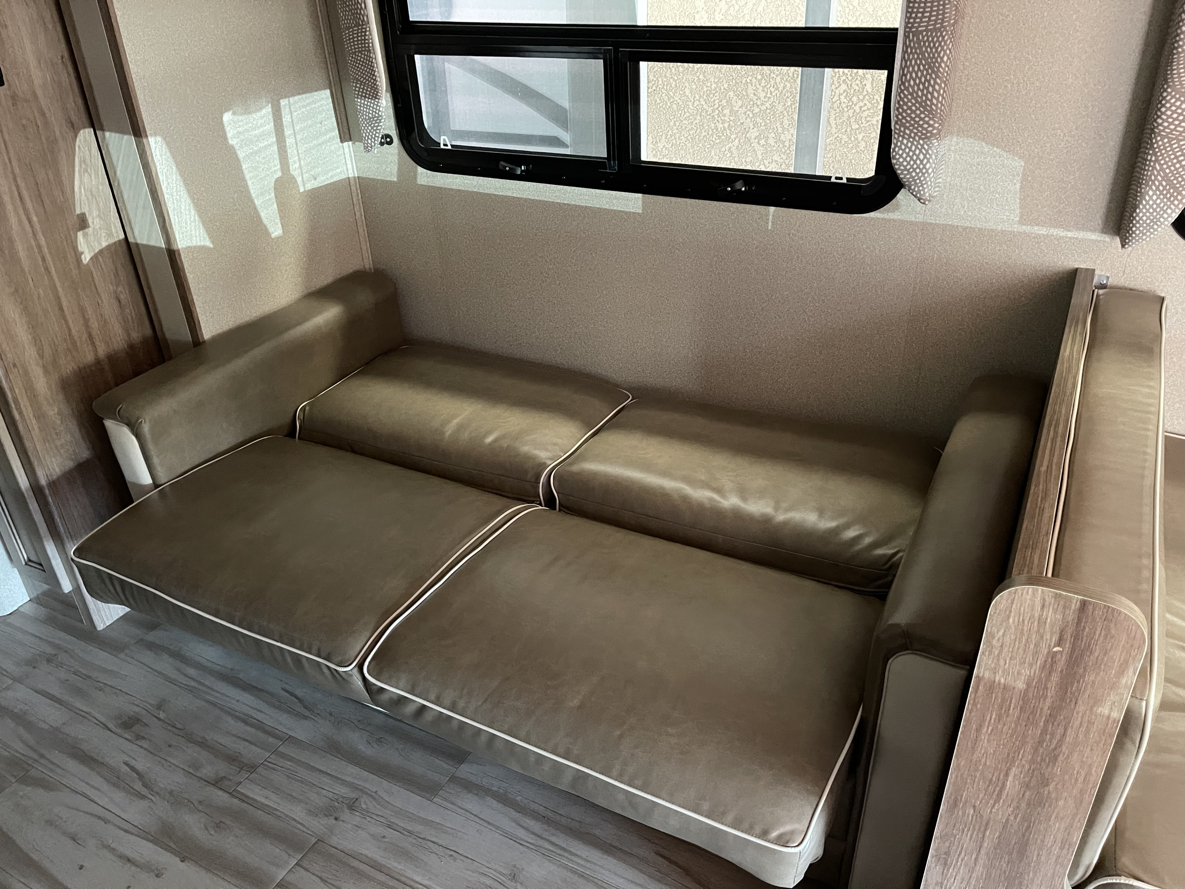 RV rental interior: Spacious brown convertible sofa with white piping, window, and wood-look floor, ideal for your next trip.. Entegra Coach Odyssey 2019
