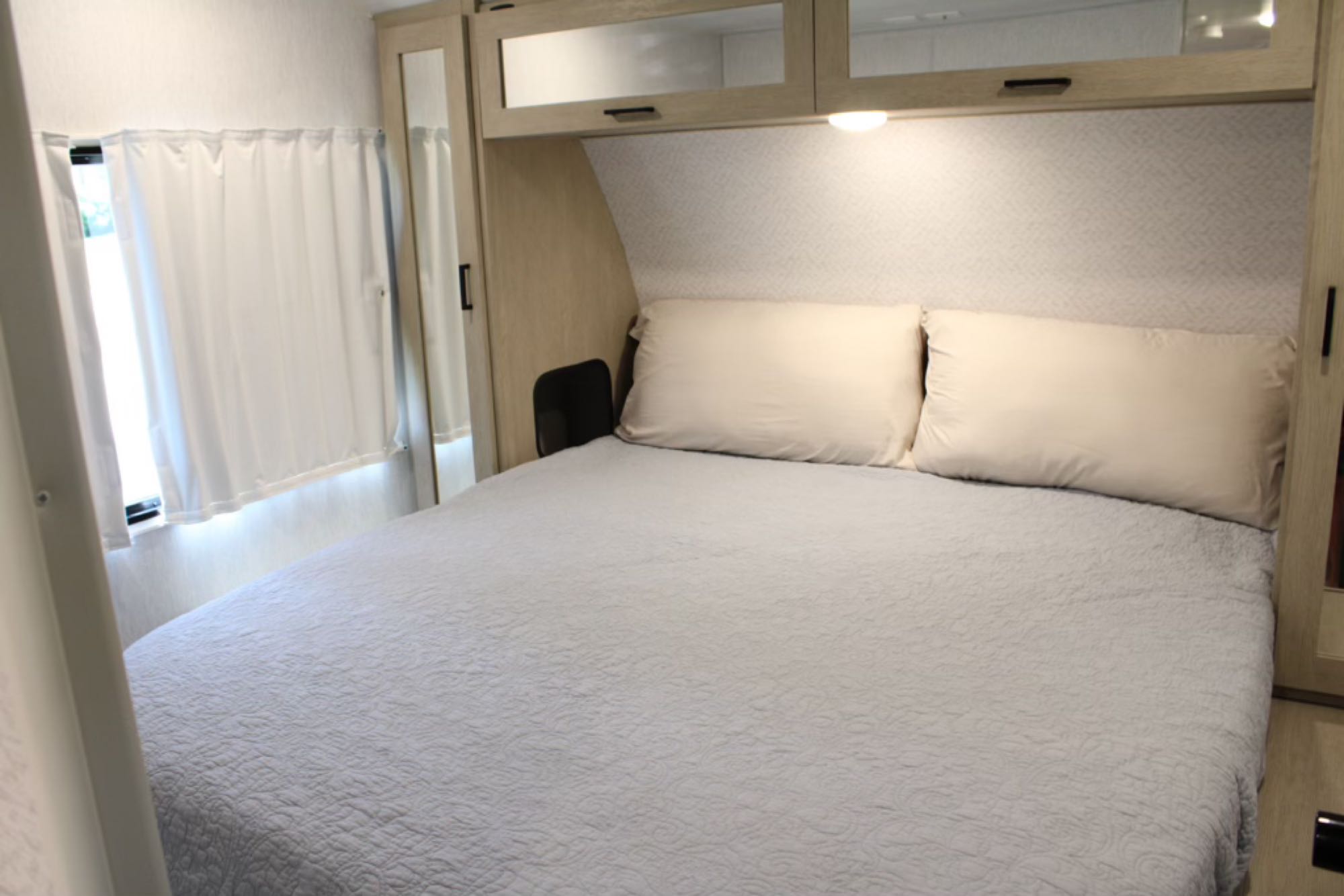 This RV rental bedroom features a comfortable bed with a quilted comforter, overhead storage, and soft lighting, perfect for travel.. Forest River Wildwood Platinum 2024