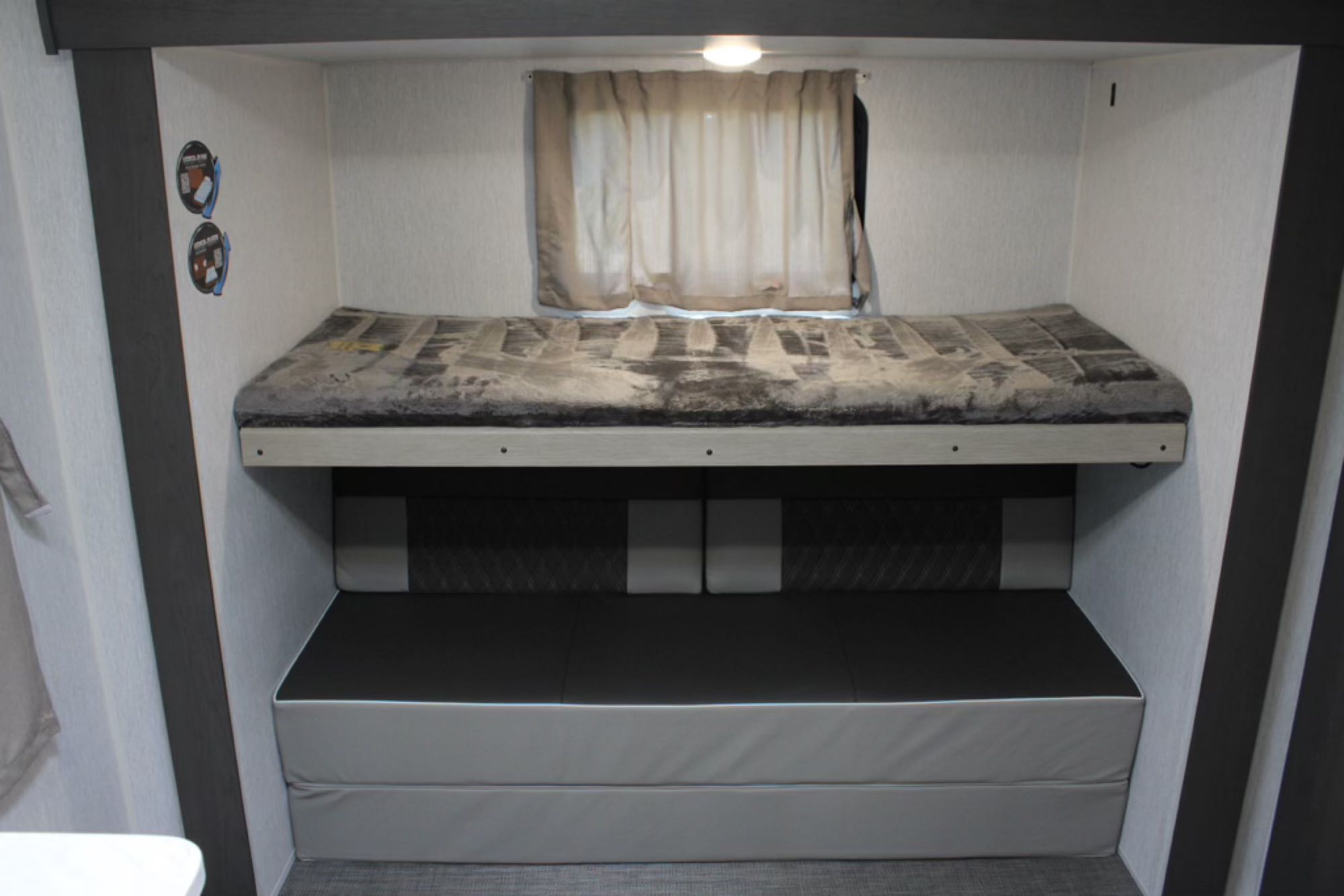 Inside an RV rental, compact bunk beds feature a top mattress with a blanket, and a dark gray convertible sofa below.. Forest River Wildwood Platinum 2024