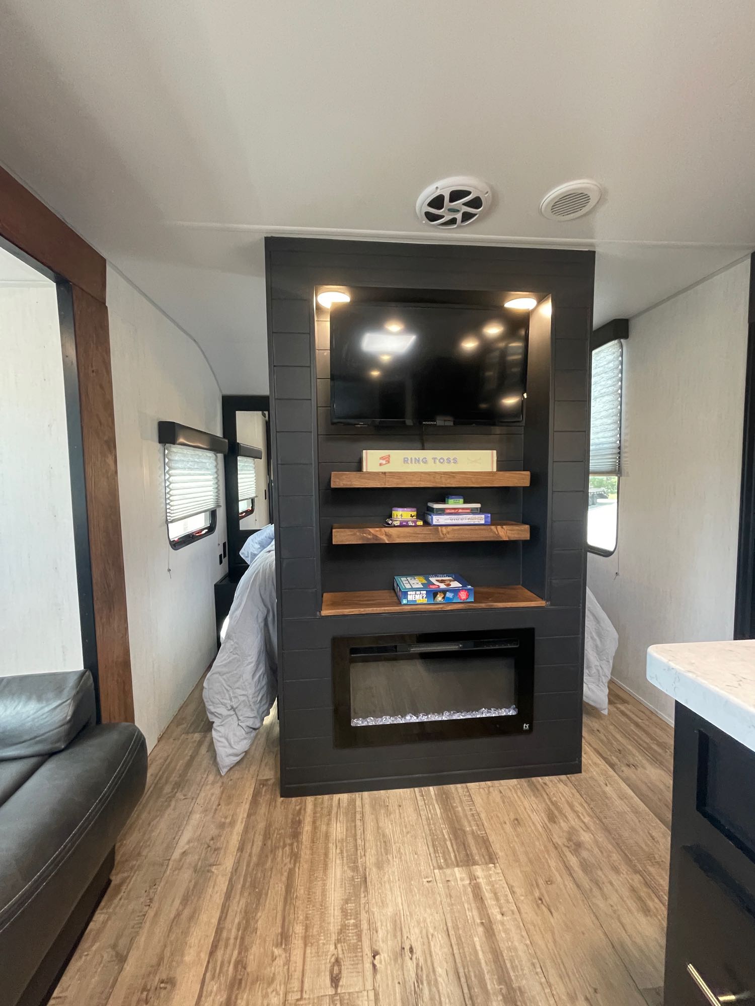 Sleek RV rental interior featuring a central entertainment wall with TV, fireplace, and shelves, separating living from bedroom.. Forest River Cherokee Grey Wolf 2022