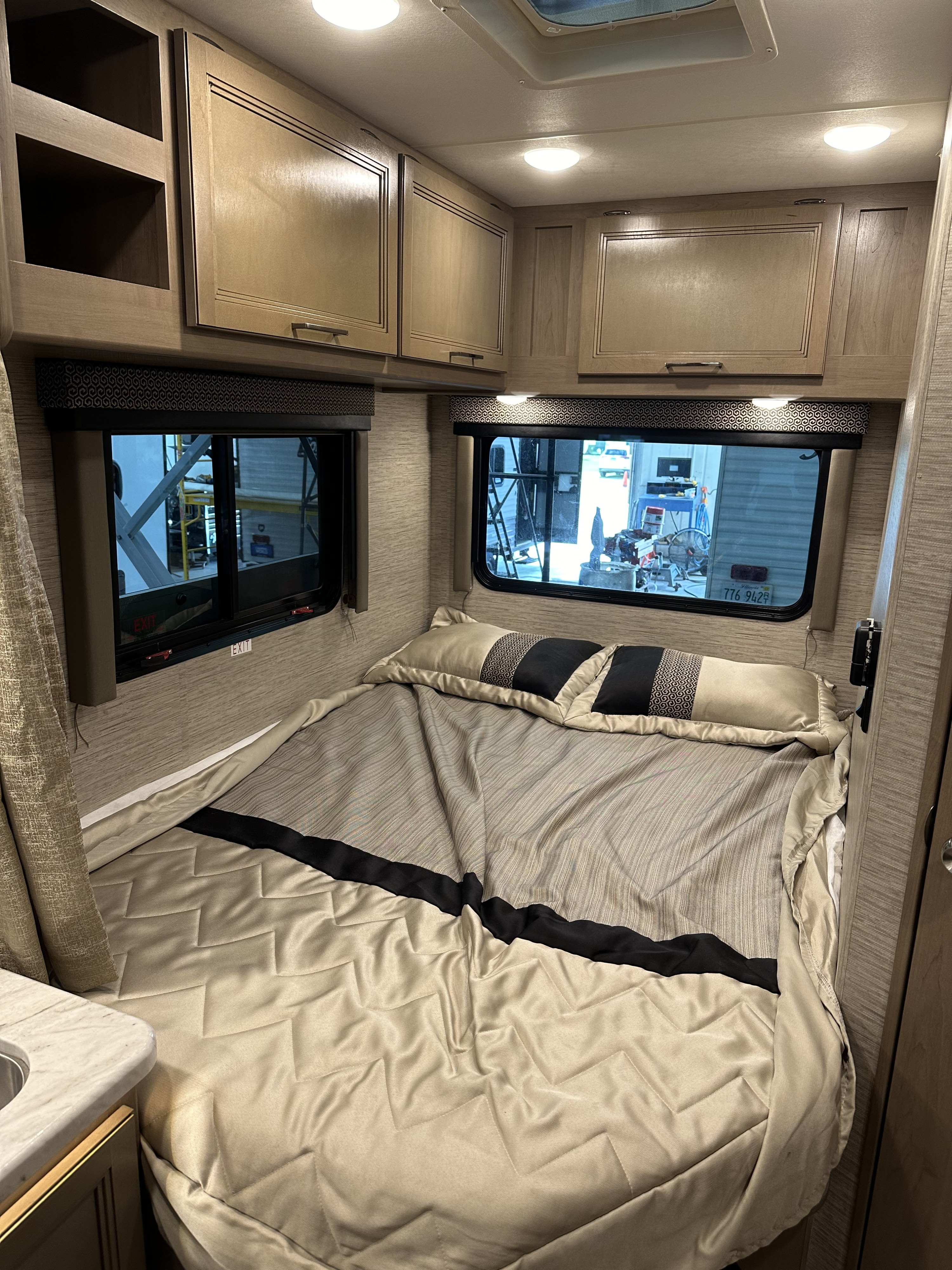Cozy RV bedroom with a comfortable bed, overhead cabinets, and windows for your next rv rental adventure.. Thor Coleman 2021