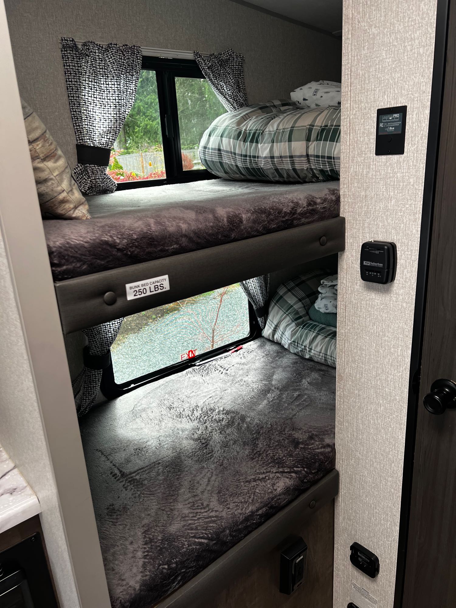 Inside an RV rental: view of stacked bunk beds with plaid and solid blankets, windows, and wall-mounted controls for comfort.. Sonic Lite 2022