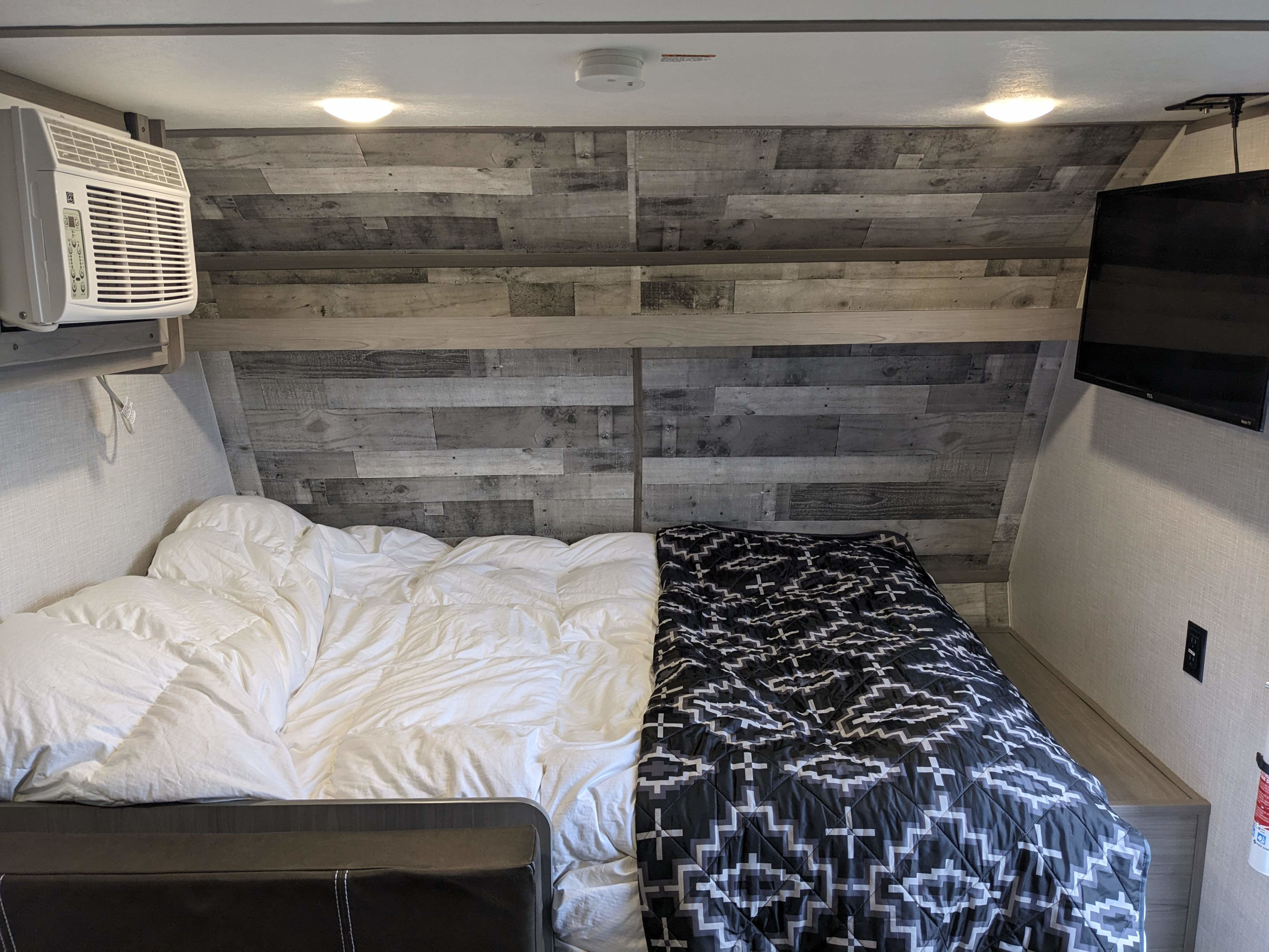 Cozy RV rental bedroom with a bed, white comforter, patterned blanket, AC unit, and TV for a comfortable stay.. Keystone RV Colman Lantern 17b 2023