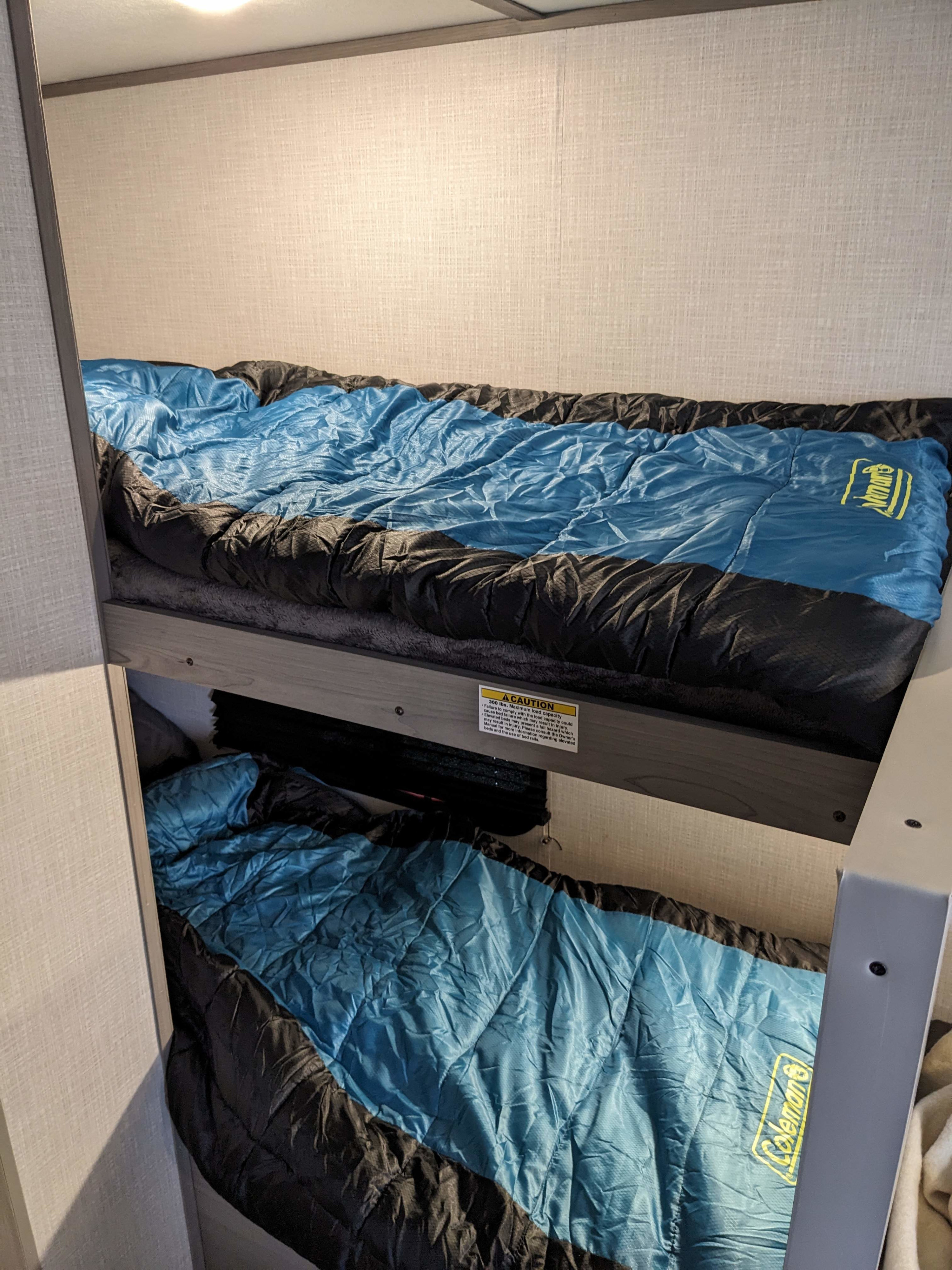 RV rental bunk beds with blue and black Coleman sleeping bags provide cozy sleeping arrangements.. Keystone RV Colman Lantern 17b 2023