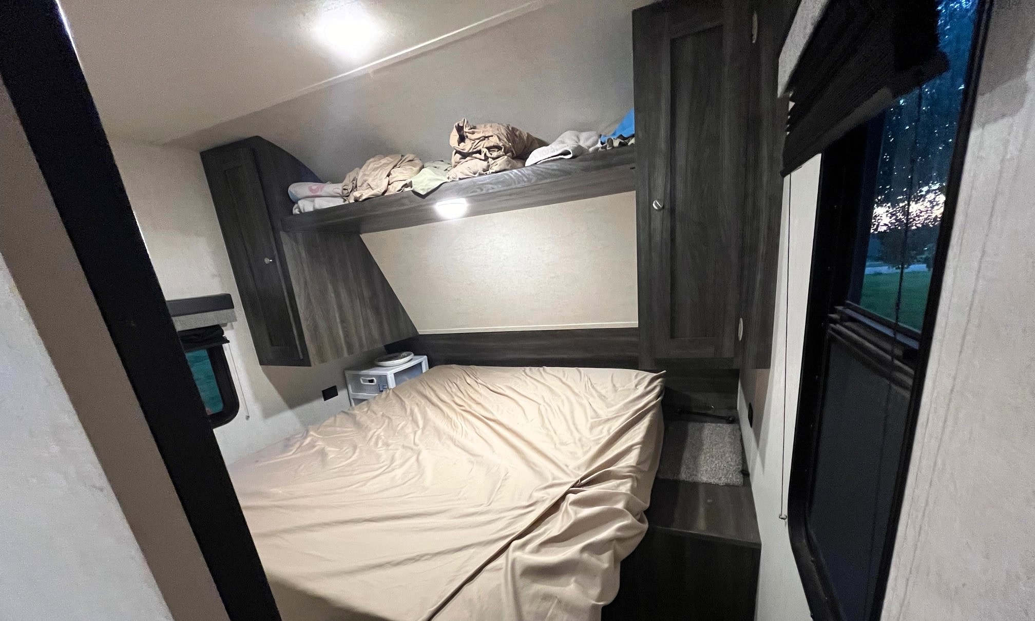 This RV rental bedroom features a lower bed, an upper bunk with linens, and dark wood built-in cabinets. Windows offer outdoor views.. Highland Ridge RV Open Range 2019
