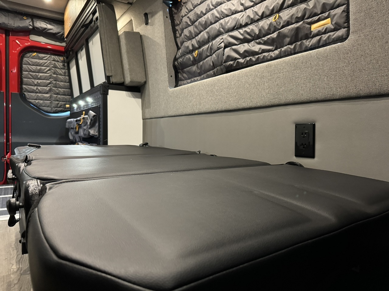 Explore this RV rental's cozy interior: modular black seating/bed, power outlet, insulated windows, ideal for mobile adventures.. Storyteller Overland Beast Mode AWD 2024