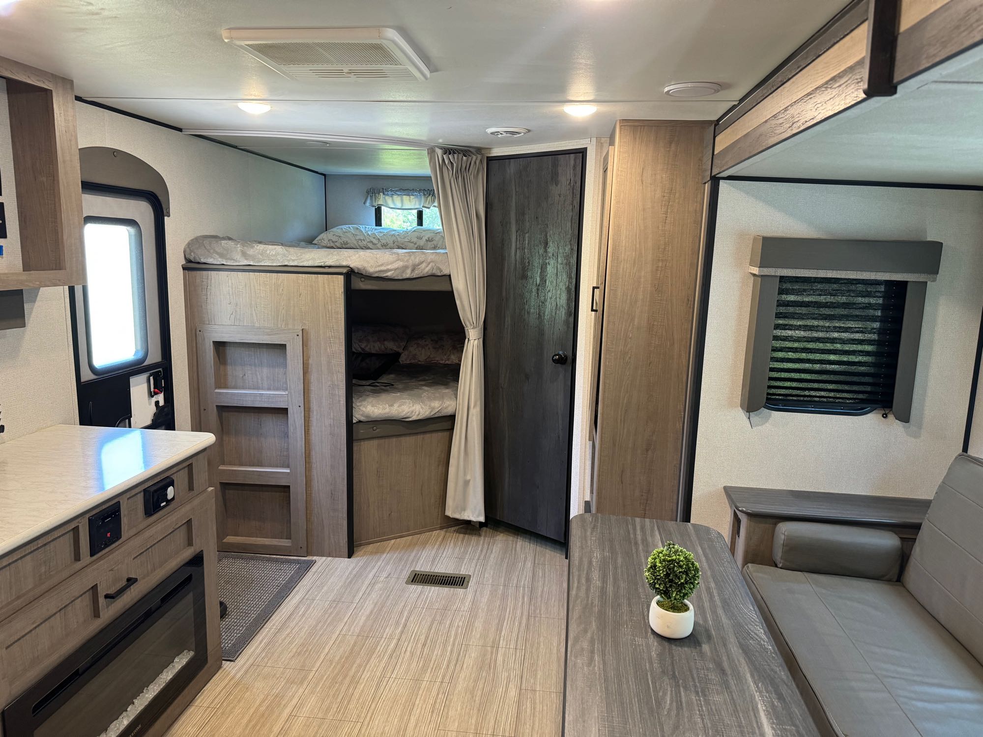 Inside a clean RV rental. Features bunk beds, a compact kitchen with fireplace, and a dining area with a sofa.. Keystone RV Hideout 2021