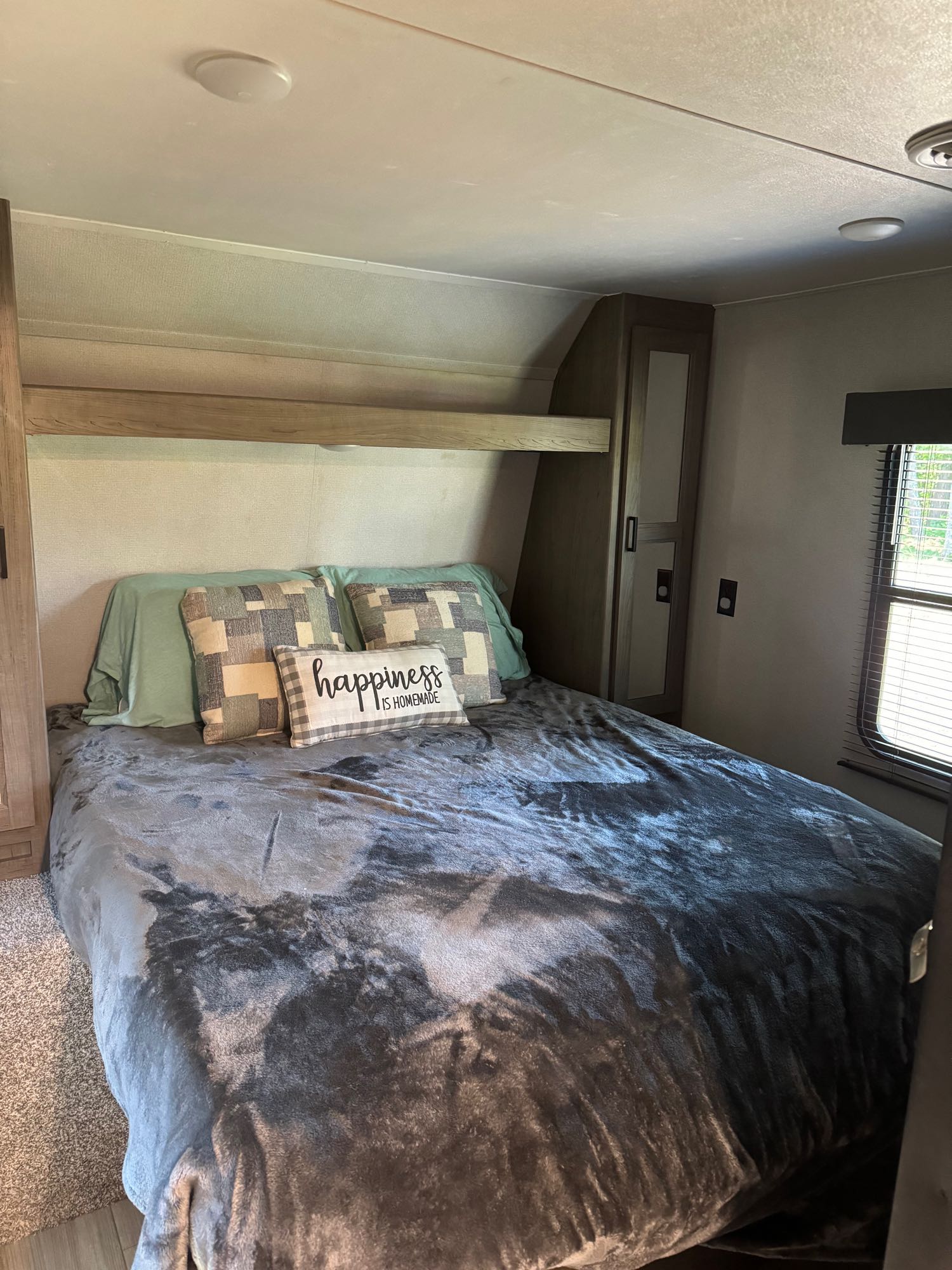 Comfortable RV rental bedroom with a cozy bed, "happiness is homemade" pillow, built-in storage, and a window.. Keystone RV Hideout 2021