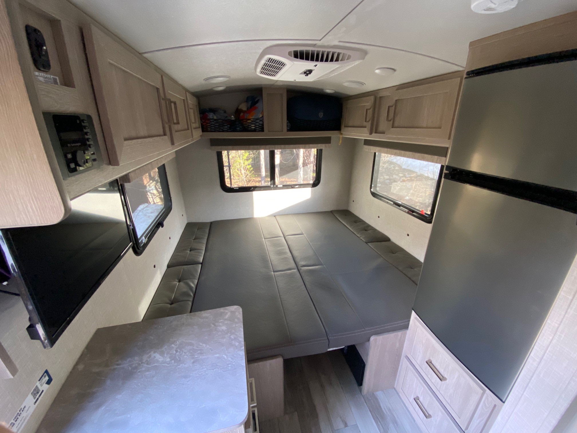 The bright interior of an RV rental features a convertible bed/lounge, overhead cabinets, a refrigerator, and control panel.. Forest River Flagstaff E-Pro 2022