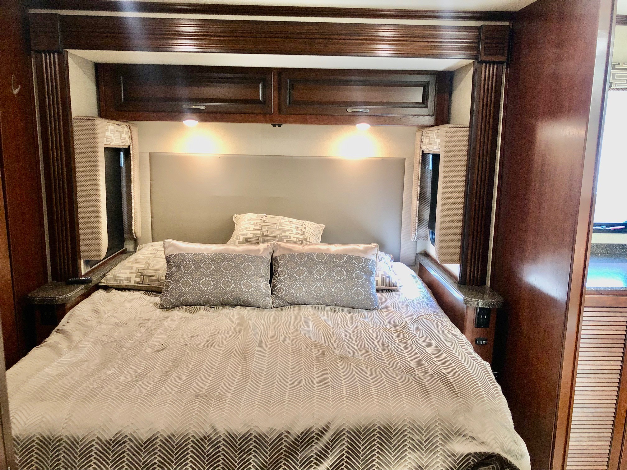 RV rental master bedroom featuring a queen bed, patterned bedding, reading lights, overhead storage, and bedside power.. Fleetwood Storm 2019