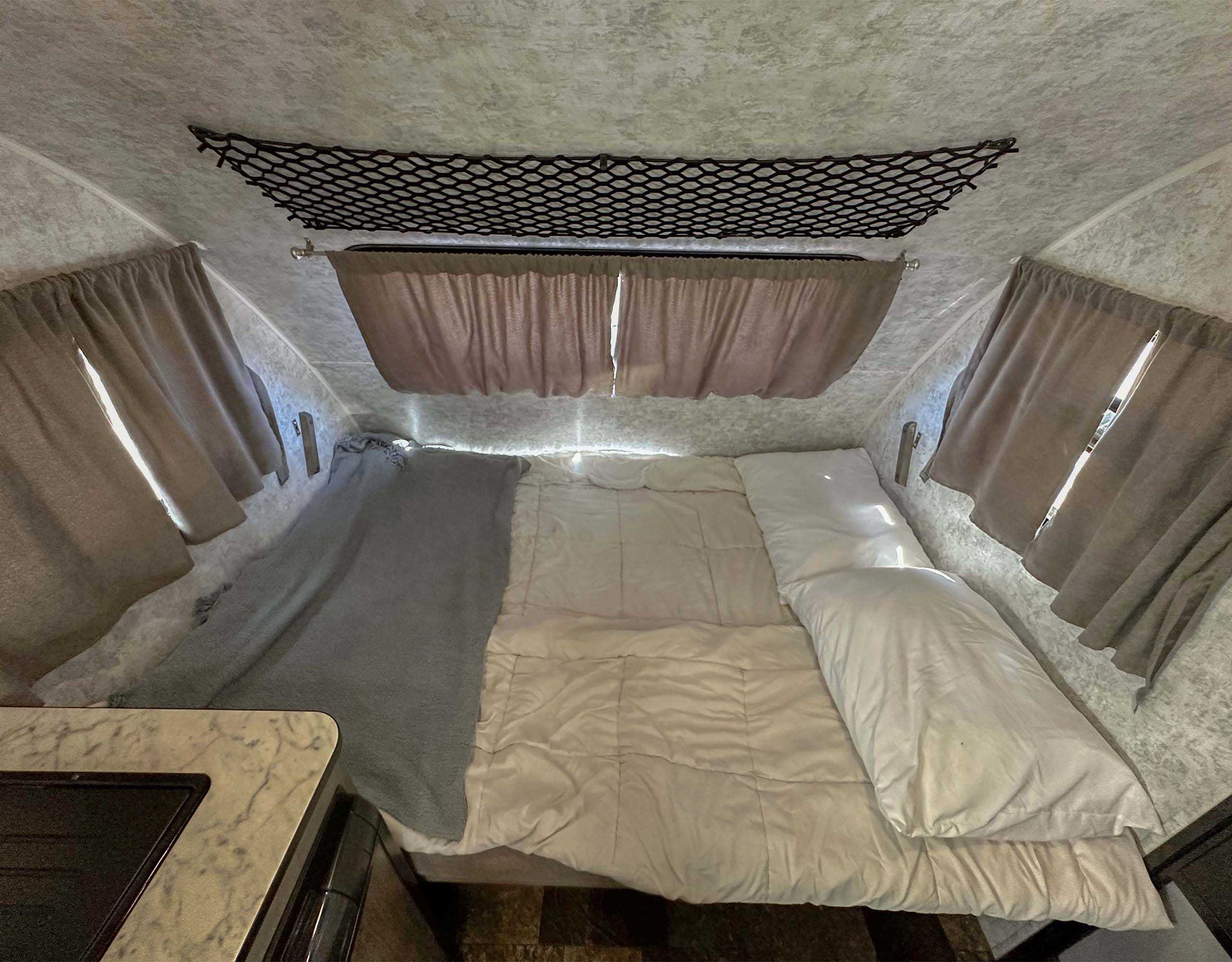 Cozy RV rental sleeping area with bed, pillows, and overhead storage net, perfect for your next adventure.. Prolite Lounge 2022