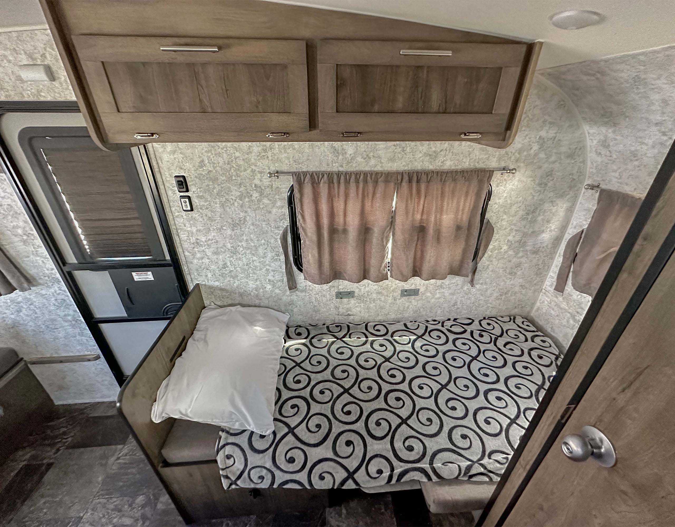 RV rental interior: A cozy bedroom with patterned bedding, overhead cabinets, and an entry door.. Prolite Lounge 2022