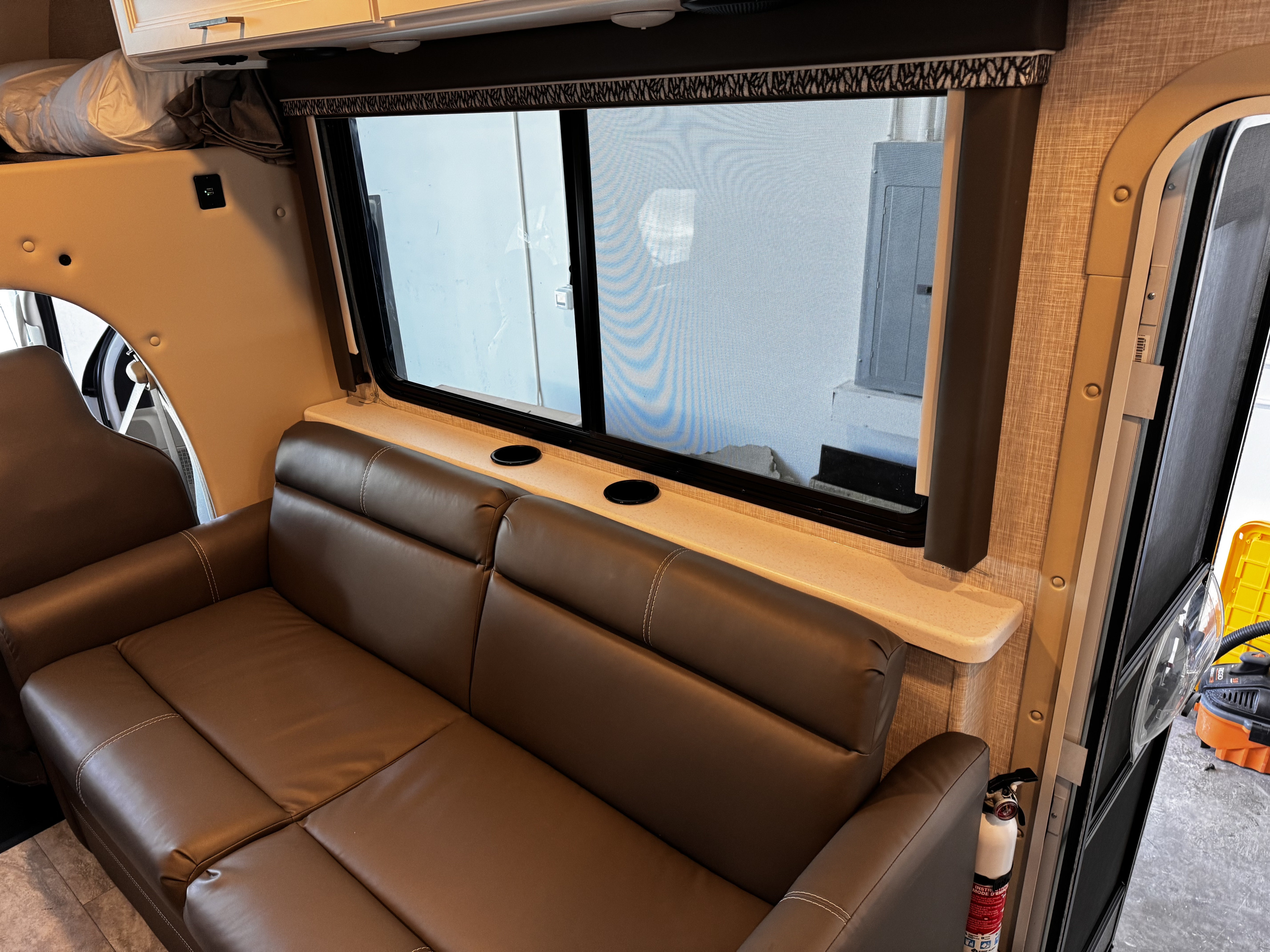 Cozy RV rental interior with a brown sofa, window, bunk bed, USB charger, and fire extinguisher for comfortable travels.. Thor Motor Coach Quantum LC28 2025