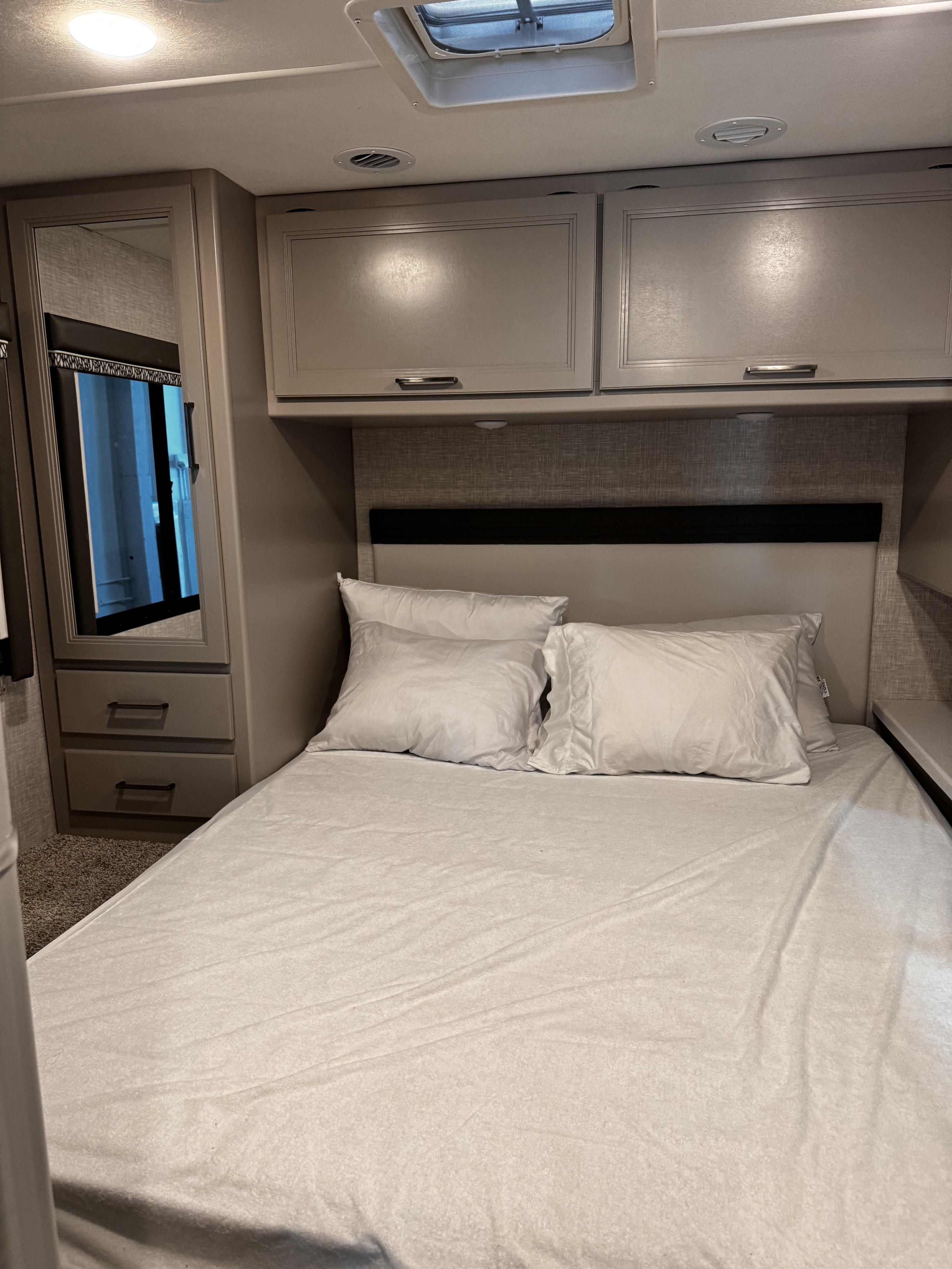Compact RV rental bedroom featuring a bed, overhead cabinets, and built-in mirror closet.. Thor Motor Coach Quantum LC28 2025