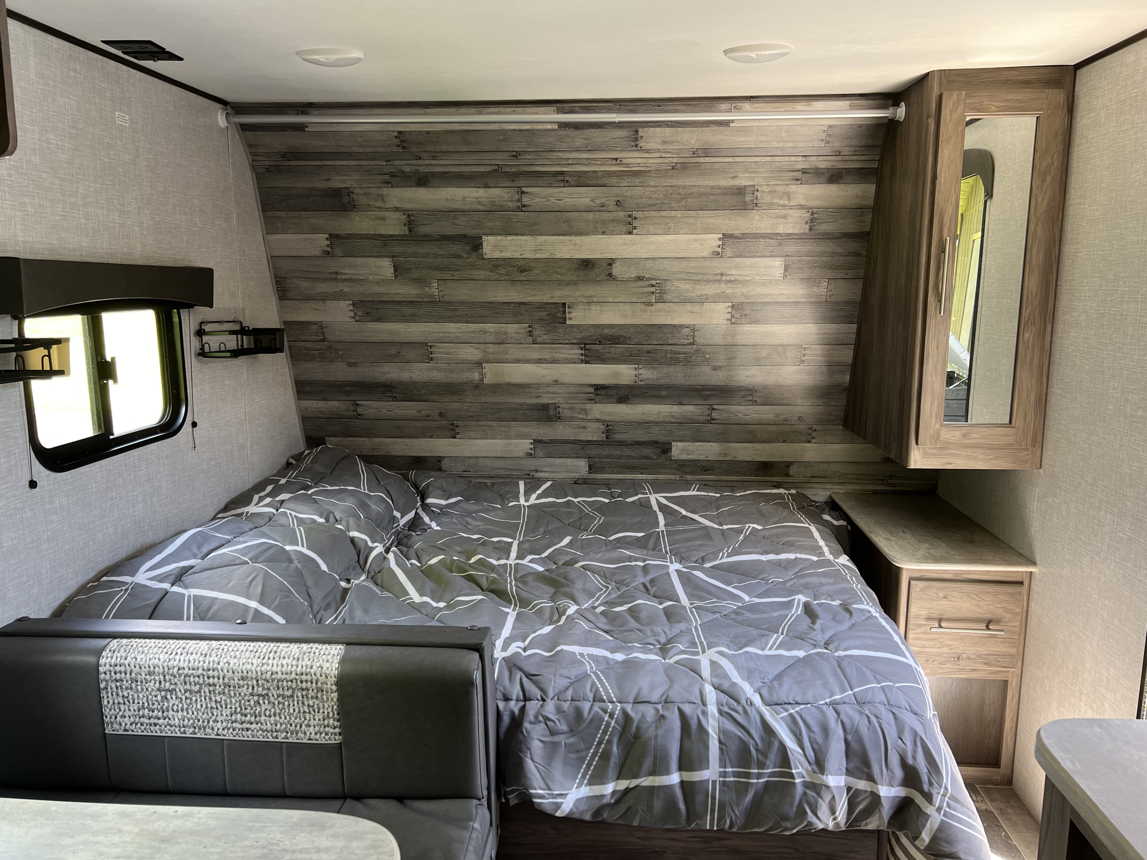 This RV rental features a comfortable bed with gray bedding, a rustic wood accent wall, and practical storage, perfect for travel.. Crossroads RV Zinger Lite 2022