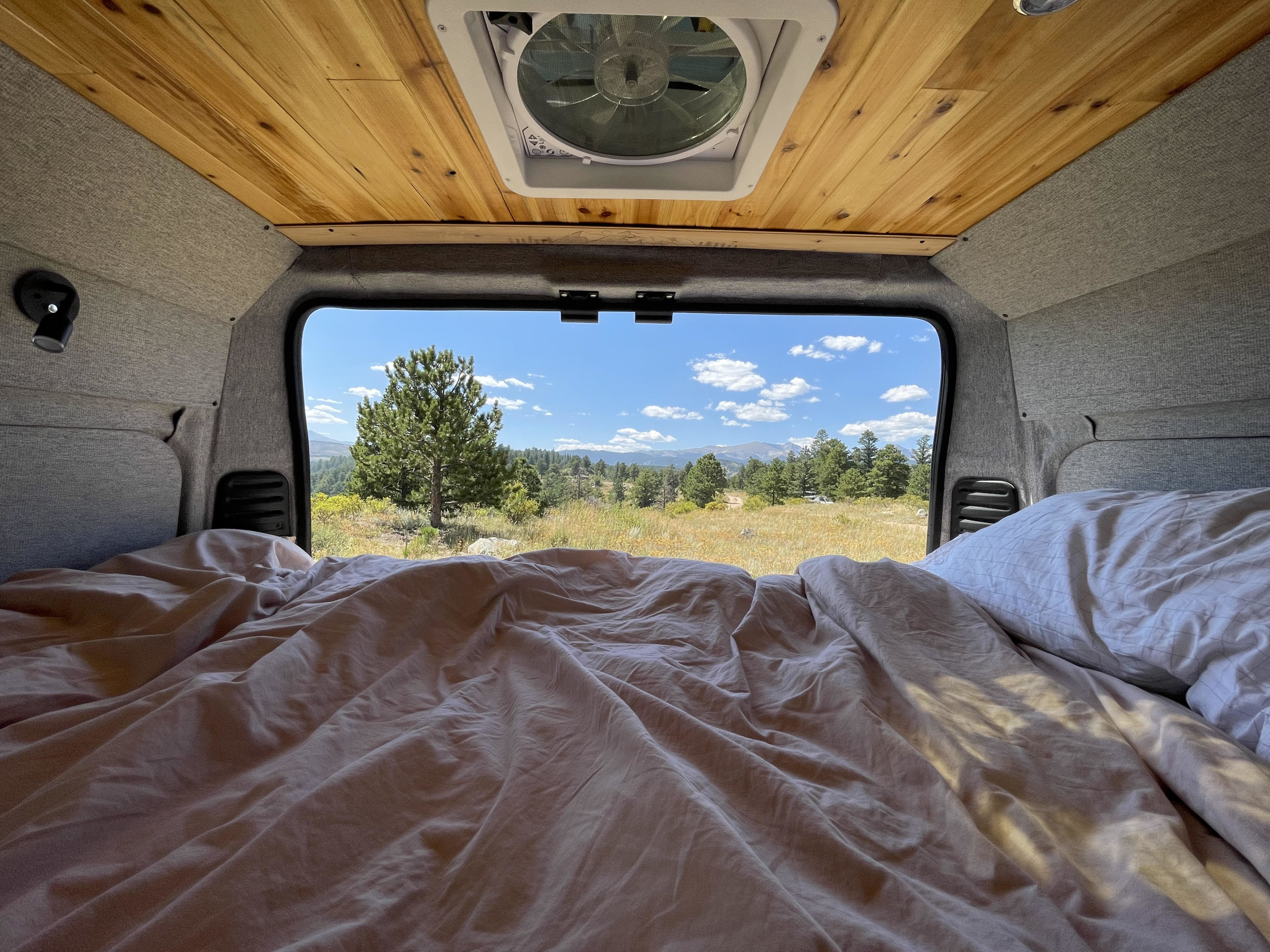 Cozy rv rental bed with a stunning view of mountains, forests, and blue sky from inside the van.. Dodge Ram 1500 2014