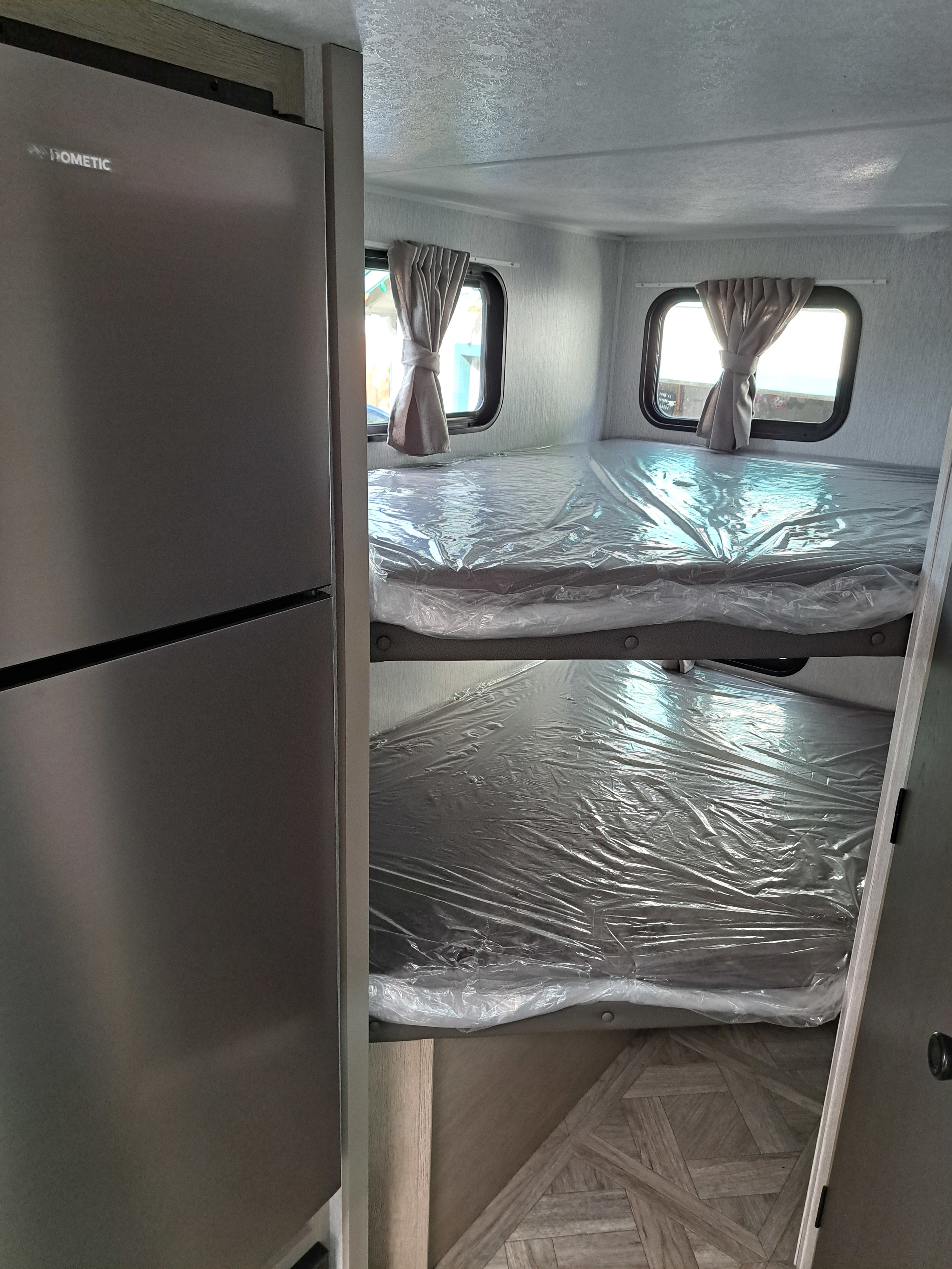 View of an RV rental's interior: Dometic refrigerator on left, two plastic-wrapped bunk beds on right.. Forest River Salem FSX 2024